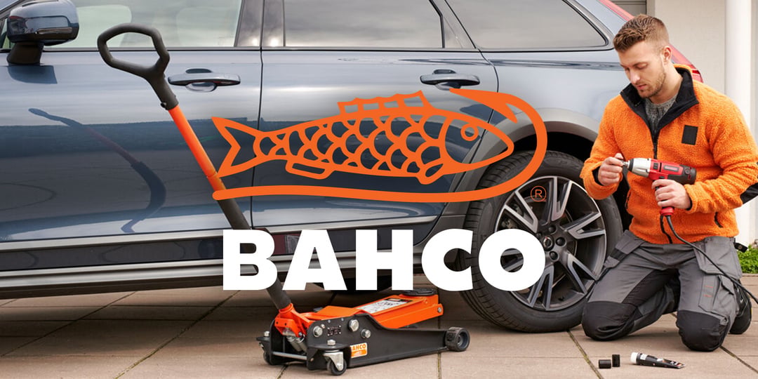 Ein Mann benutzt ein Elektrowerkzeug in der Nähe des Vorderrads eines blauen Geländewagens, der von einem orangefarbenen Wagenheber mit dem BAHCO-Logo und fetter Schrift angehoben wird.
