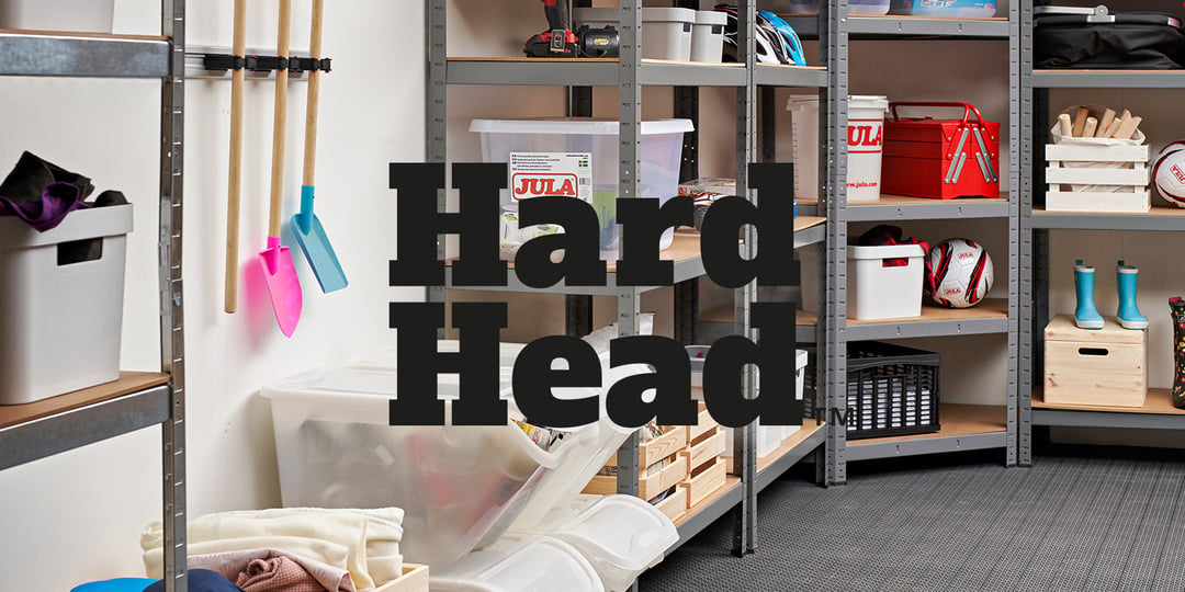 Lagerrom med metallhyller fulle av esker, sportsutstyr og husholdningsartikler; hageredskaper på veggen. "Hard Head" i fet, svart tekst.