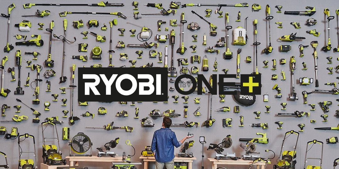 Työpöydän ääressä istuva henkilö kohtaa siististi järjestetyn Ryobi ONE+ -työkaluseinän, jonka yläpuolella on keskellä tuotemerkin logo.
