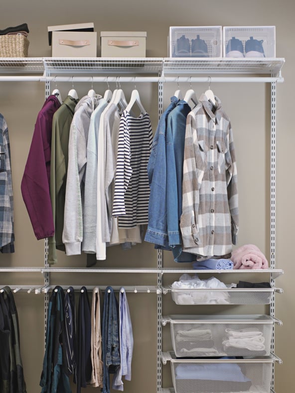 En ryddig garderobe med skjorter, gensere og jakker hengende på hvite kleshengere, oppbevaringsbokser og sko på de øverste hyllene, kurver og brettede klær på de nederste hyllene og skjerf eller belter hengende under.
