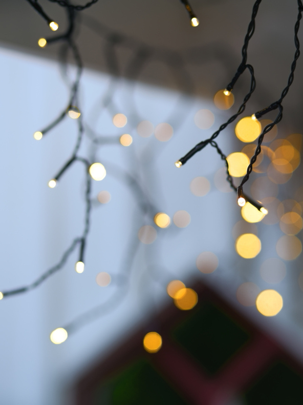 Nahaufnahme von Lichterketten mit winzigen leuchtenden Glühbirnen, die im Hintergrund sanft verschwommen sind, um einen Bokeh-Effekt auf einem neutralen Hintergrund zu erzielen.