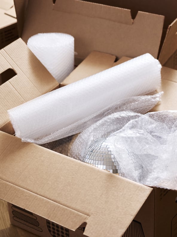 En öppen kartong innehåller flera rullar bubbelplast och en spegelriktad discokula som är delvis inslagen, vilket indikerar packning för förvaring eller flytt.