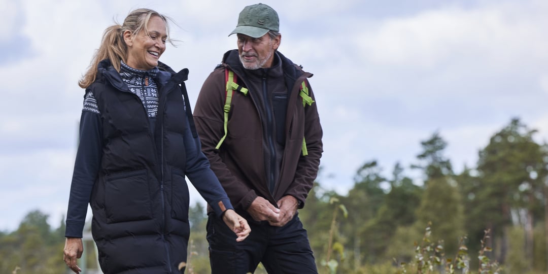 En man och en kvinna i utomhuskläder promenerar tillsammans utomhus.