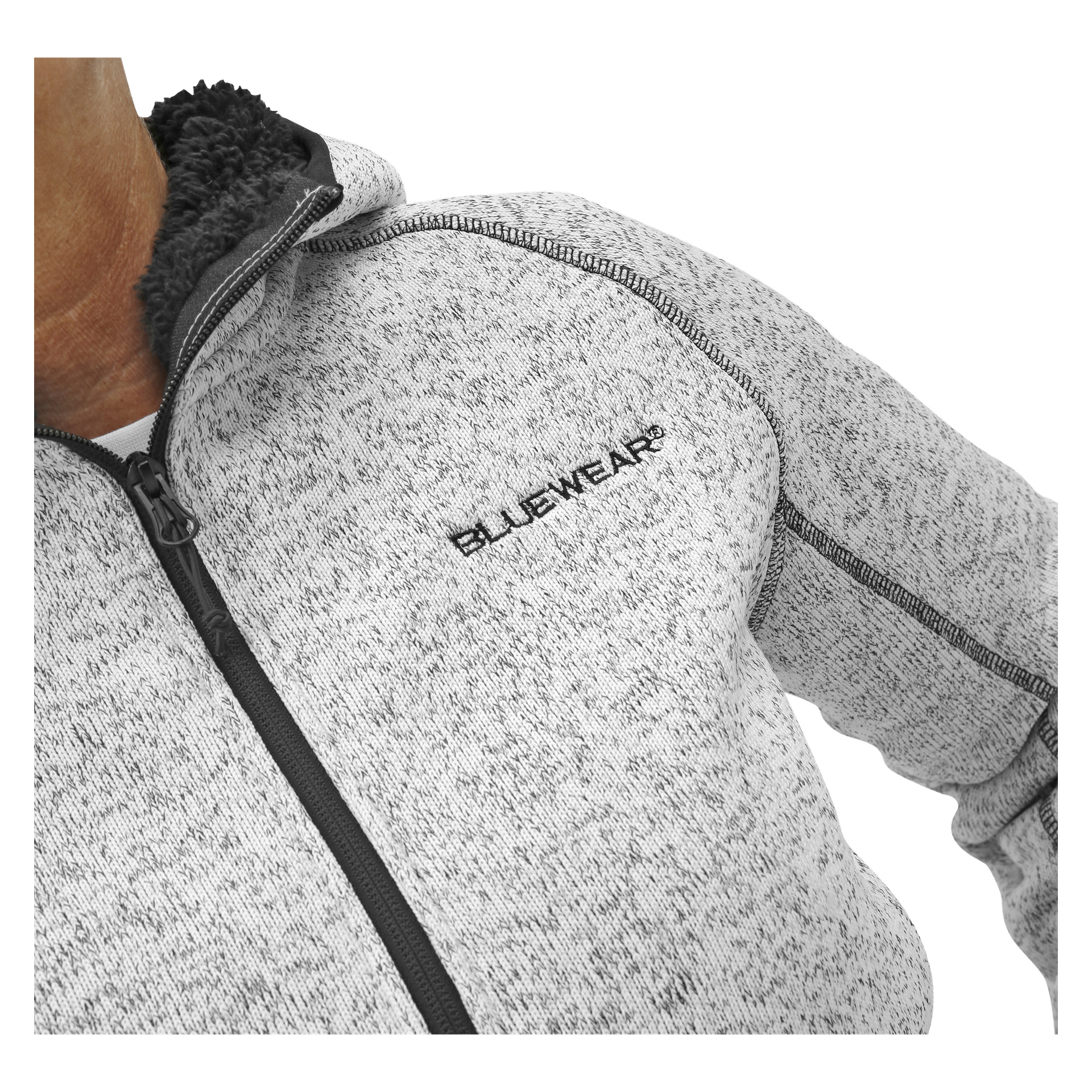 En person har på seg en lysegrå damestrikket fleecejakke fra Bluewear, med svart kant, synlig søm og BLUEWEAR brodert på brystet. Kun overkroppen er synlig.