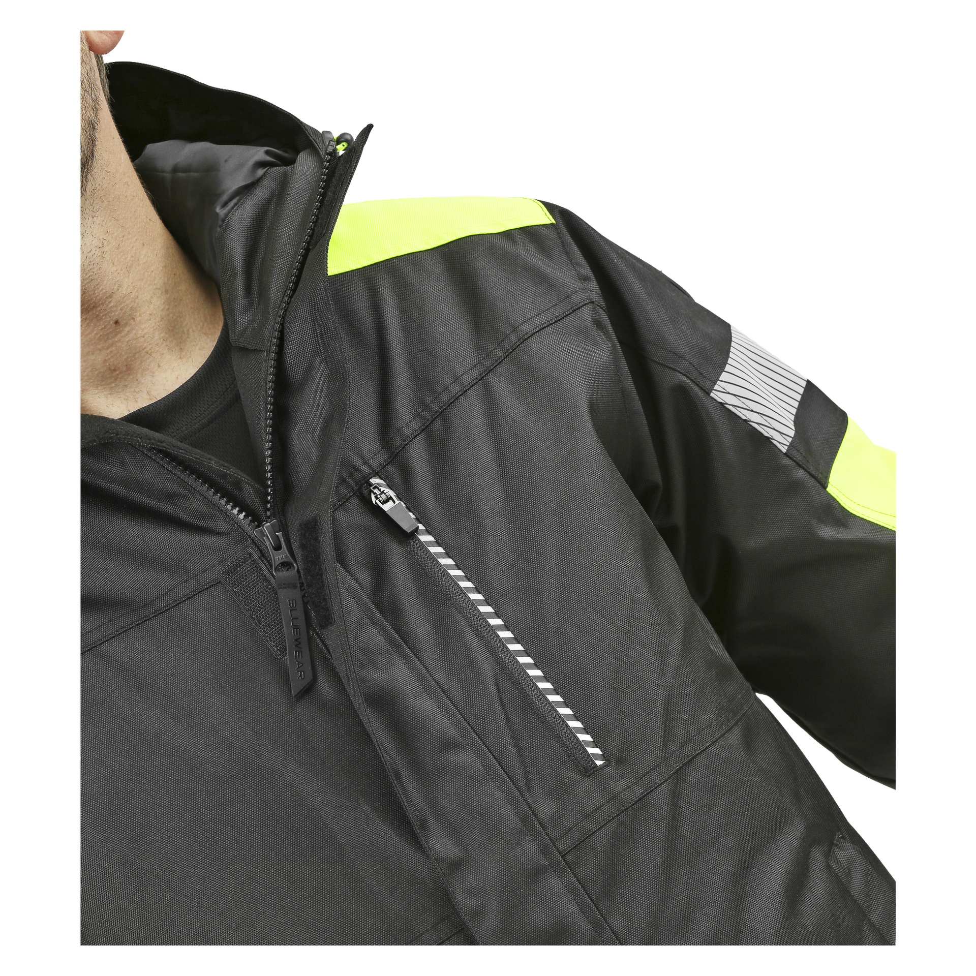 En person syns i Bluewear Parka, som har reflekterande detaljer, gula detaljer och en ficka med dragkedja på bröstet. Bara en del av deras ansikte och axel syns.