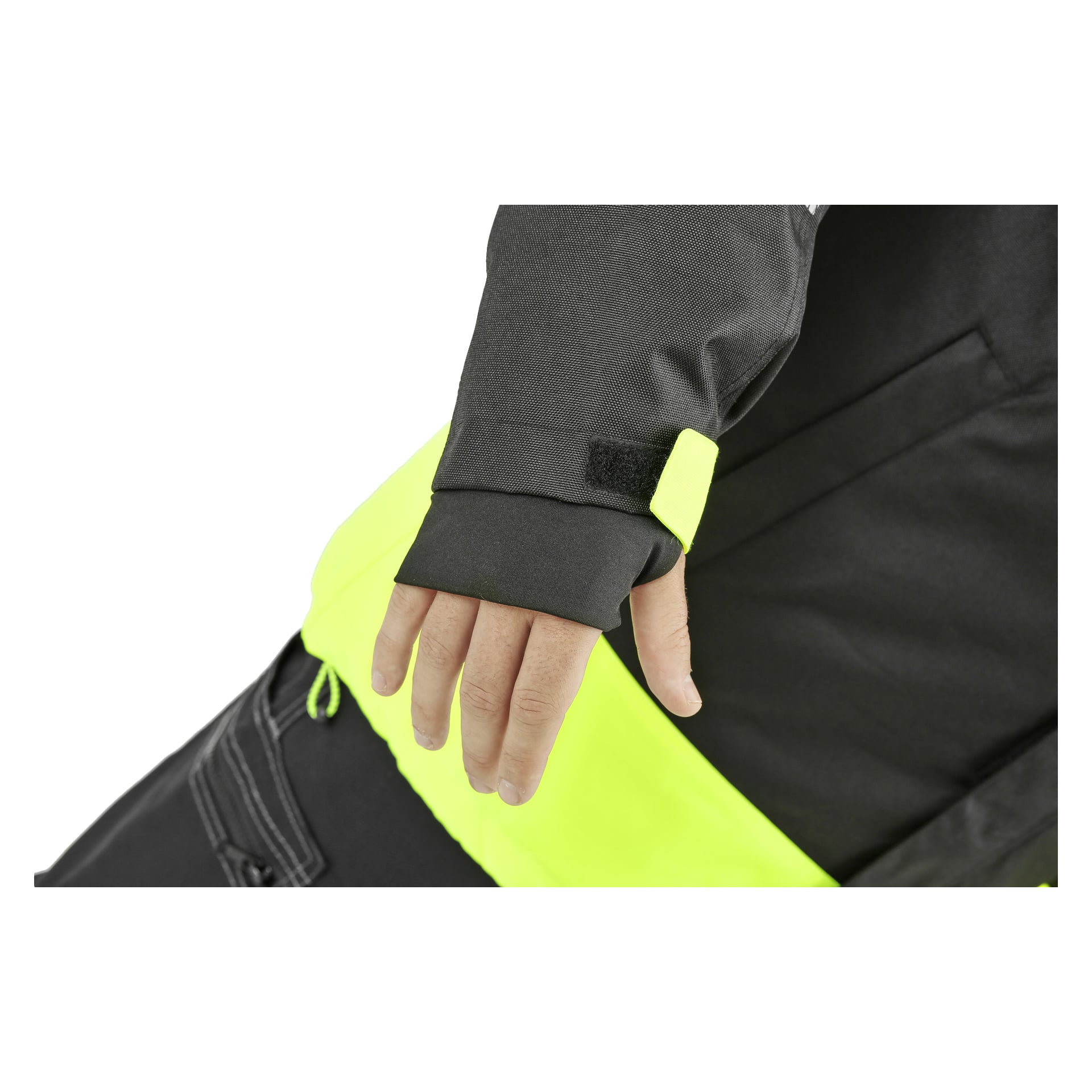 En närbild på en persons vänstra hand visar dem bära Bluewear Parka, som har reflekterande detaljer och en svart och neongul färgskala. Ärmen har en tumhålsmanschett och en justerbar kardborreband. Mer av parkasen och matchande byxor syns i bakgrunden.