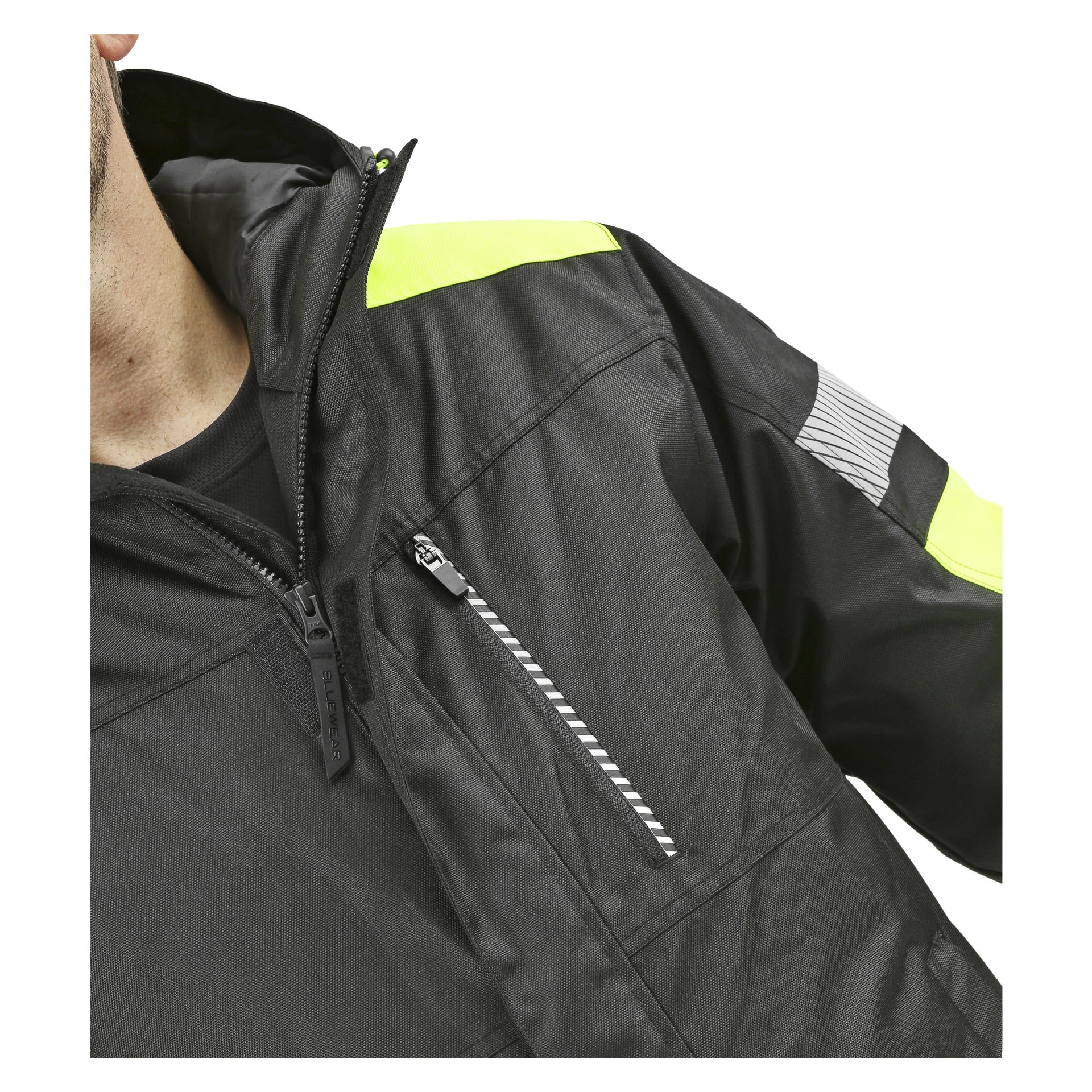Man modellerar Bluewear Parka, som har reflekterande detaljer, gula detaljer på axlarna och en bröstficka med en randig flik på dragkedjan.