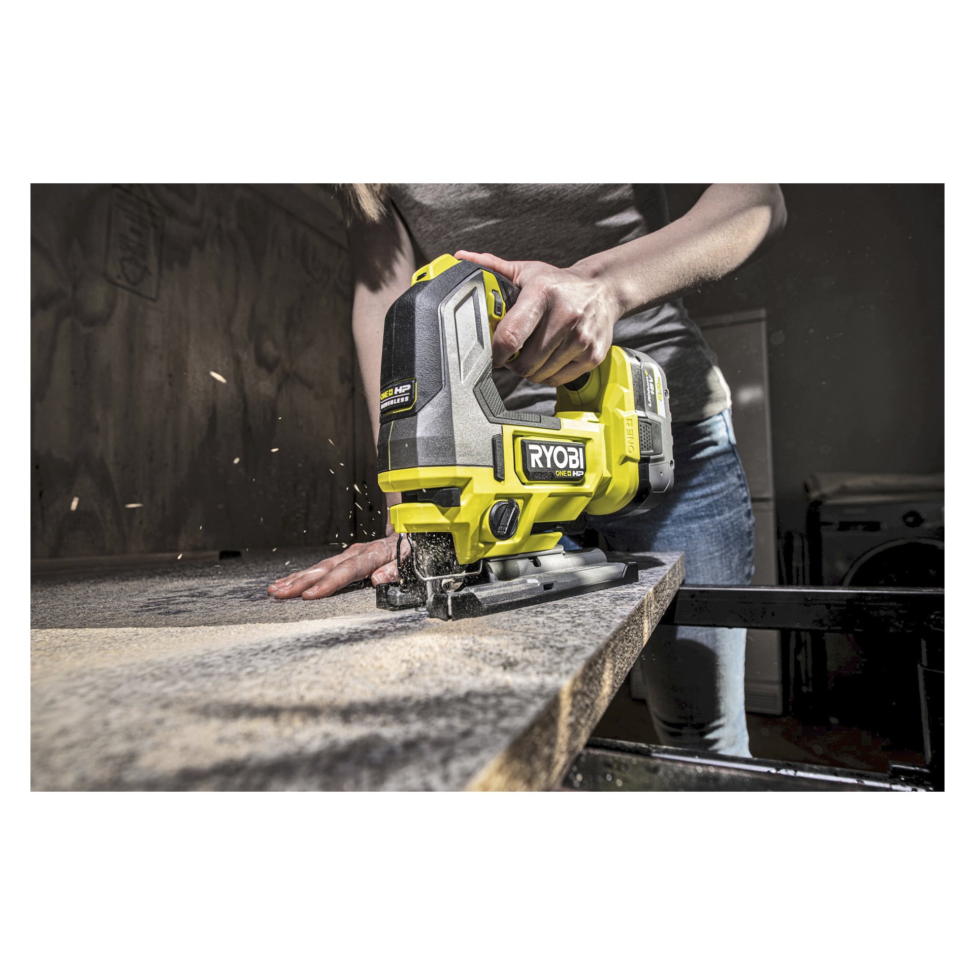 Ktoś tnie drewno wyrzynarką Ryobi One+ HP RJS18X-0, tworząc rozprysk trocin. Lewą ręką trzyma drewno stabilnie, a prawą prowadzi wyrzynarkę. Sceneria wygląda jak warsztat lub garaż.