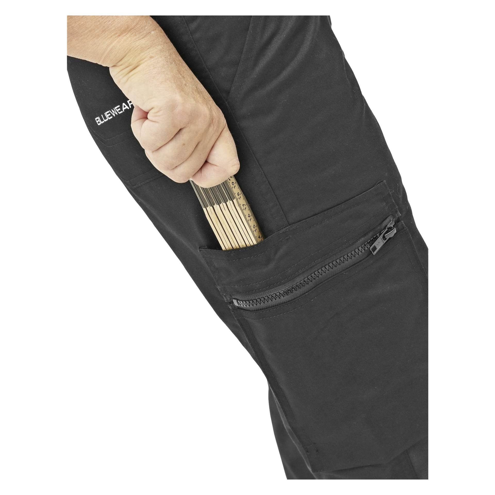 Eine Person, die schwarze Damen-Servicehosen von Bluewear trägt, steckt ein Klapplineal in eine Seitentasche mit Reißverschluss. Ihre Hand, das Lineal und ein Teil der Hose sind sichtbar.