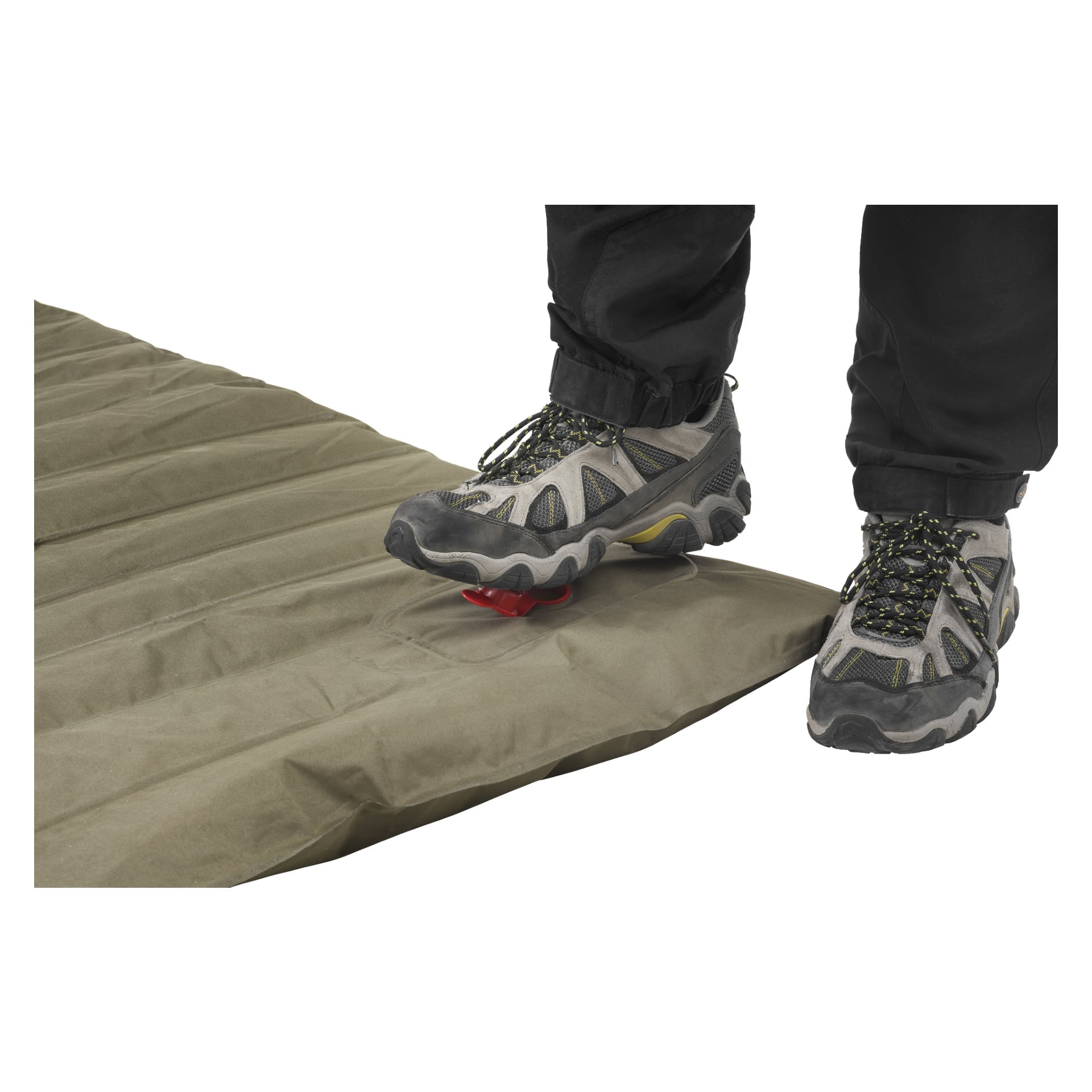 En person i tursko står på et olivengrønt Kayoba Outdoor Inflatable underlagsteppe, og bruker foten til å trykke på en rød ventil. Kun leggene og føttene vises, og underlaget er laget av solid stoff.