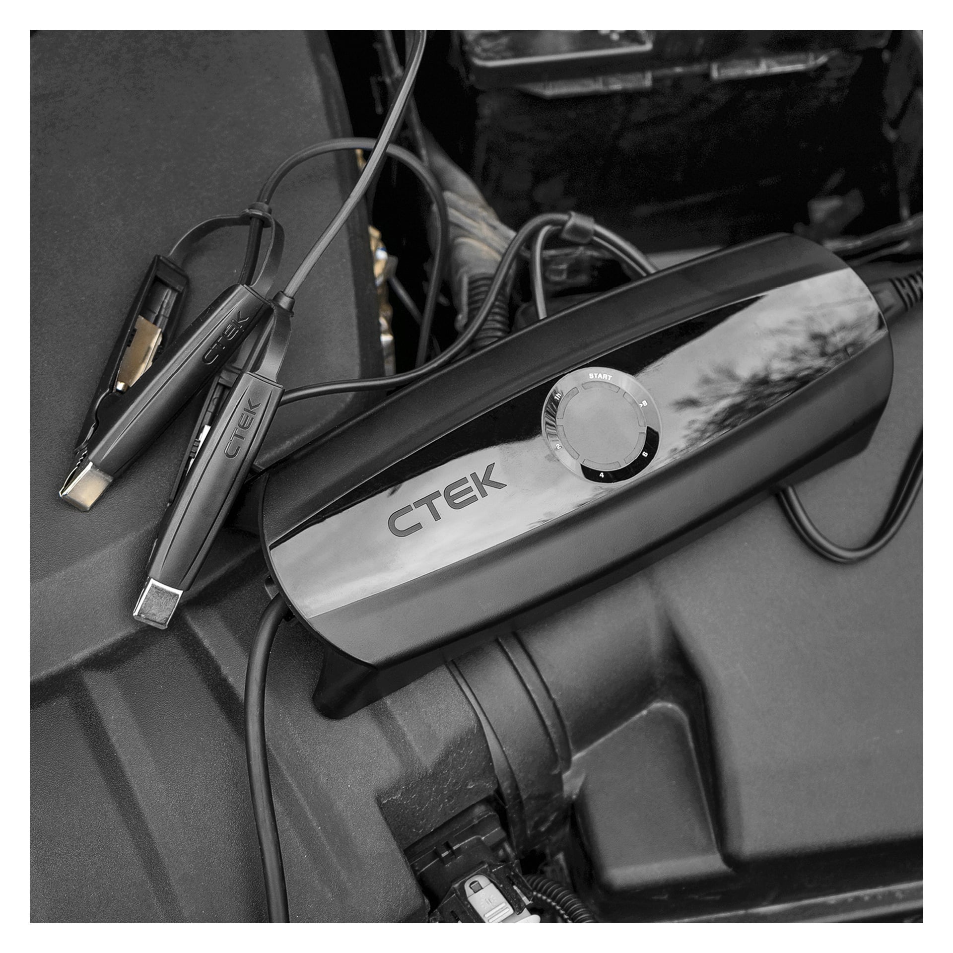 En CTEK CS ONE-batteriladdare, med sina kablar och klämmor anslutna, sitter ovanpå bilens motorkåpa. Laddarens ratt pekar på startinställningen.