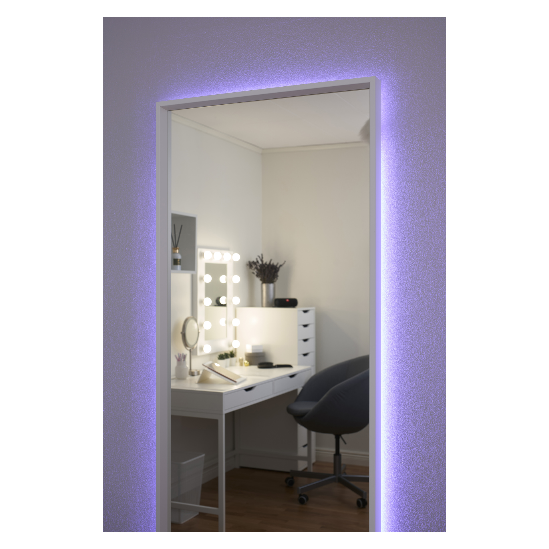 Ein Make-up-Schreibtisch in einem ordentlichen, sanft beleuchteten Raum verfügt über einen Wandspiegel, der von Anslut RGB LED-Streifen beleuchtet wird und so eine farbenfrohe Atmosphäre schafft. Der Bereich umfasst einen beleuchteten Waschtischspiegel, Schubladen zur Aufbewahrung und einen grauen Stuhl. Weiße Wände und Holzböden vervollständigen den ordentlichen Raum.