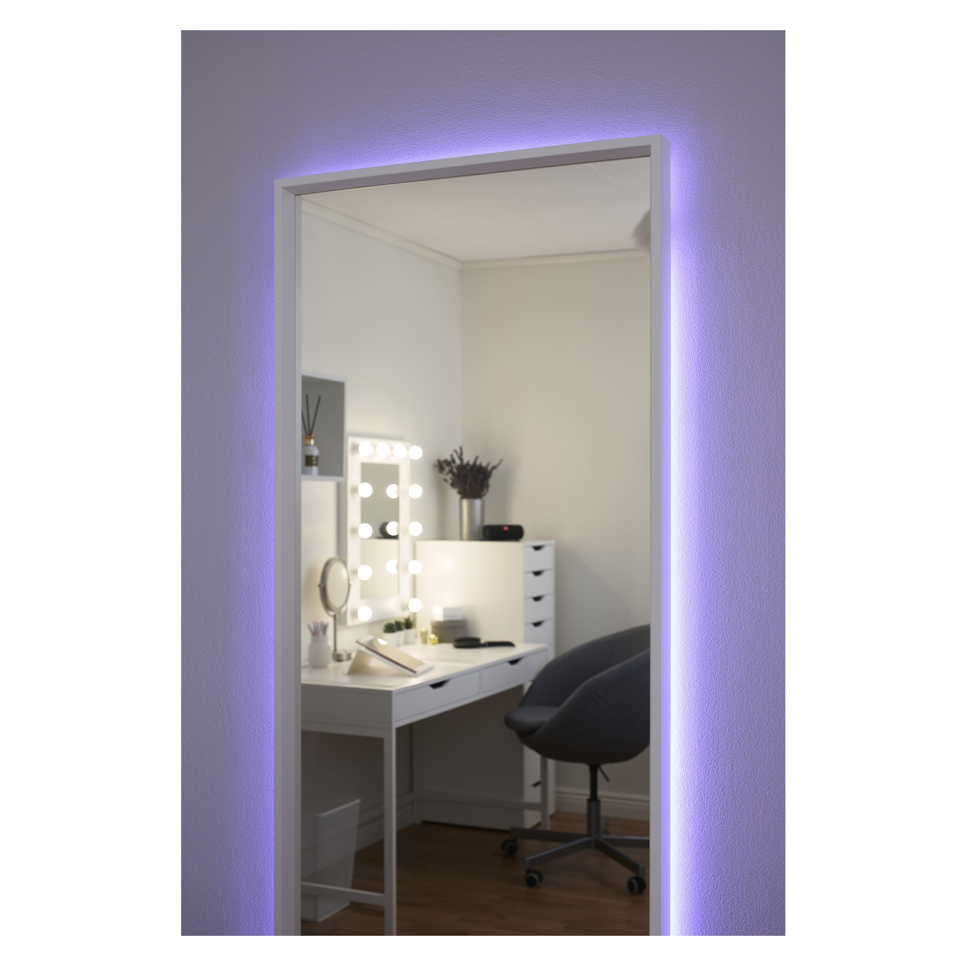Duże lustro ścienne z taśmą LED Anslut RGB emituje fioletową poświatę, odbijając schludny biały toaletnik z podświetlanym lustrem, kosmetykami, krzesłem i dekoracjami w delikatnie oświetlonym pomieszczeniu.