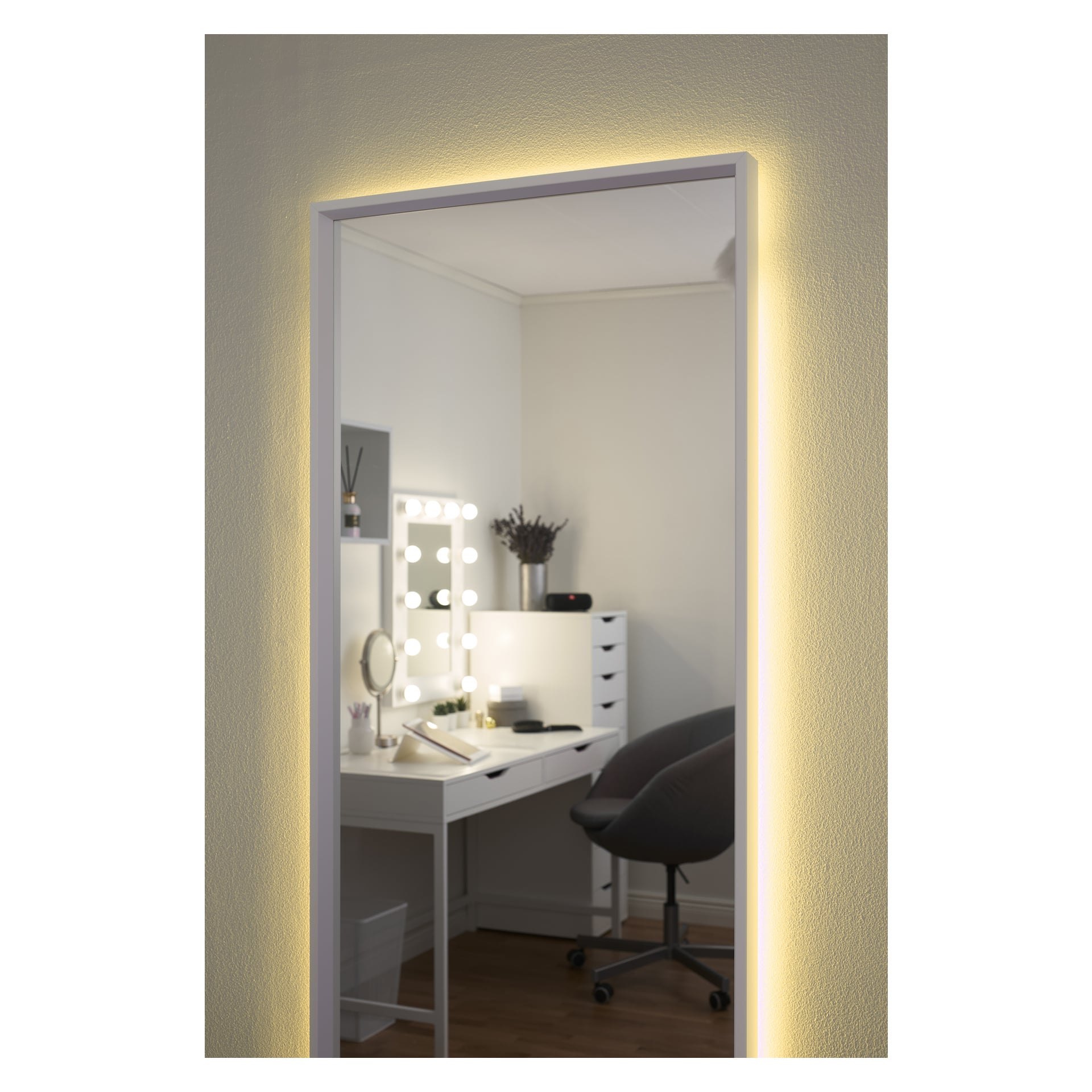 Lustro ścienne Anslut RGB LED, emitujące miękkie podświetlenie, odbija uporządkowany pokój z białym toaletką z lustrem podświetlanym żarówką, szarym fotelem, szufladami i różnymi ozdobnymi elementami.