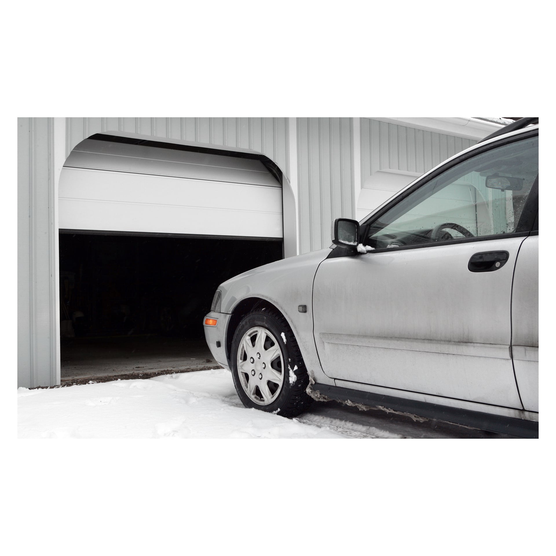 Ein silbernes Auto steht in verschneiter Umgebung vor einer offenen Garage mit weißer vertikaler Verkleidung. Das Garagentor ist teilweise angehoben, wird mit einer Hard Head-Fernbedienung bedient, und das schwach beleuchtete Innere ist sichtbar.