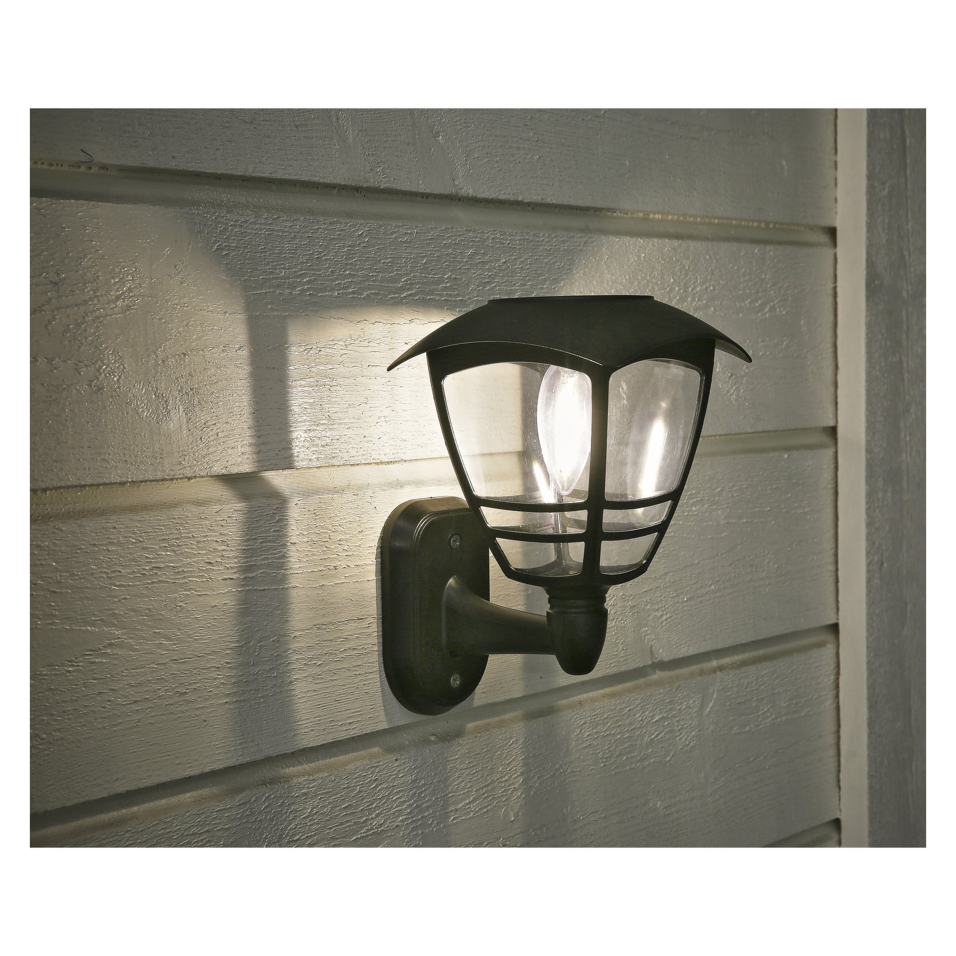 LED z lampą ścienną Anslut jest montowany na beżowej poziomej elewacji, podświetlany, rzucając cienie i oświetlając przestrzeń na zewnątrz.