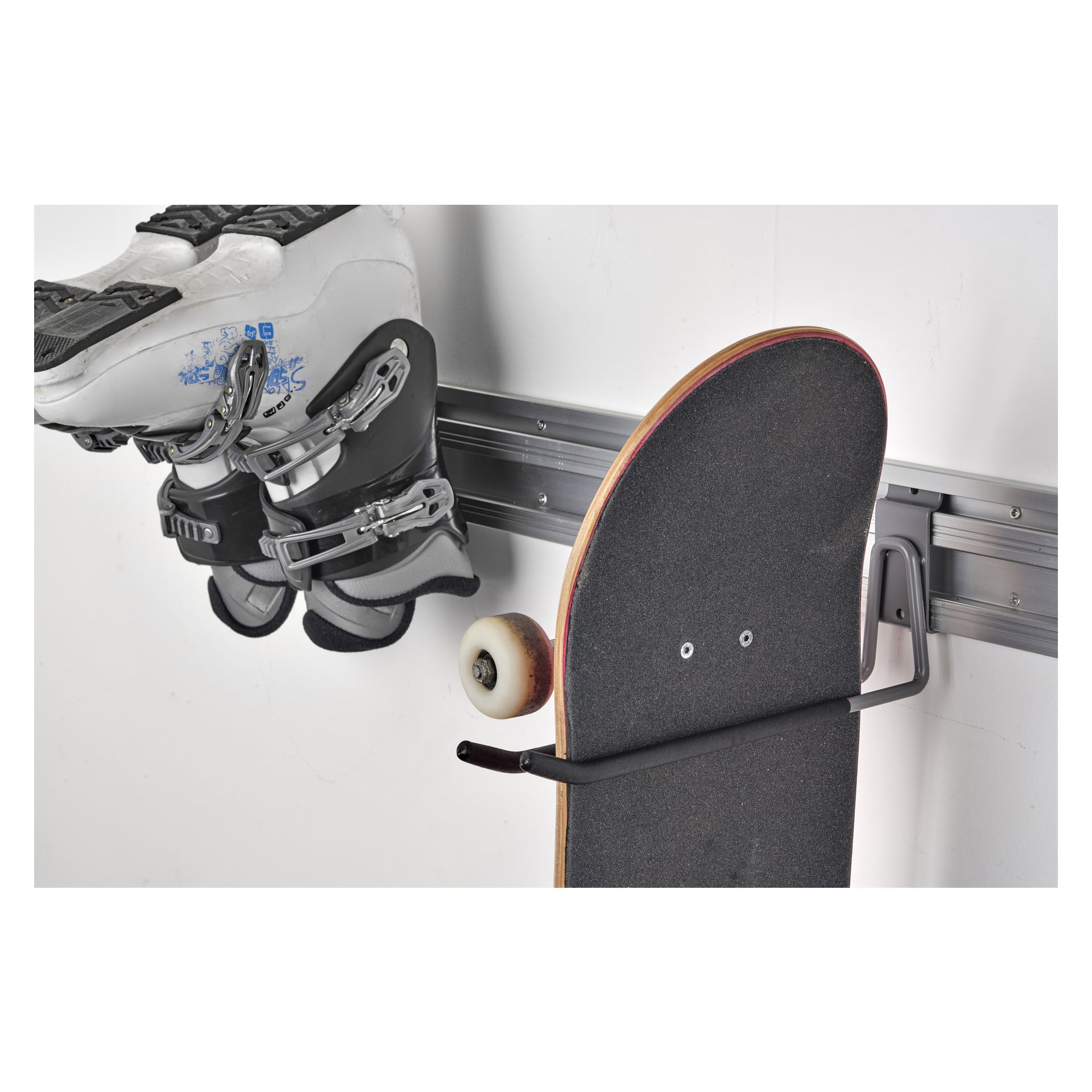 En Hard Head Holder är monterad på en vägg och håller ett par vita skridskor och en skateboard från krokar för att snyggt organisera sportutrustning.