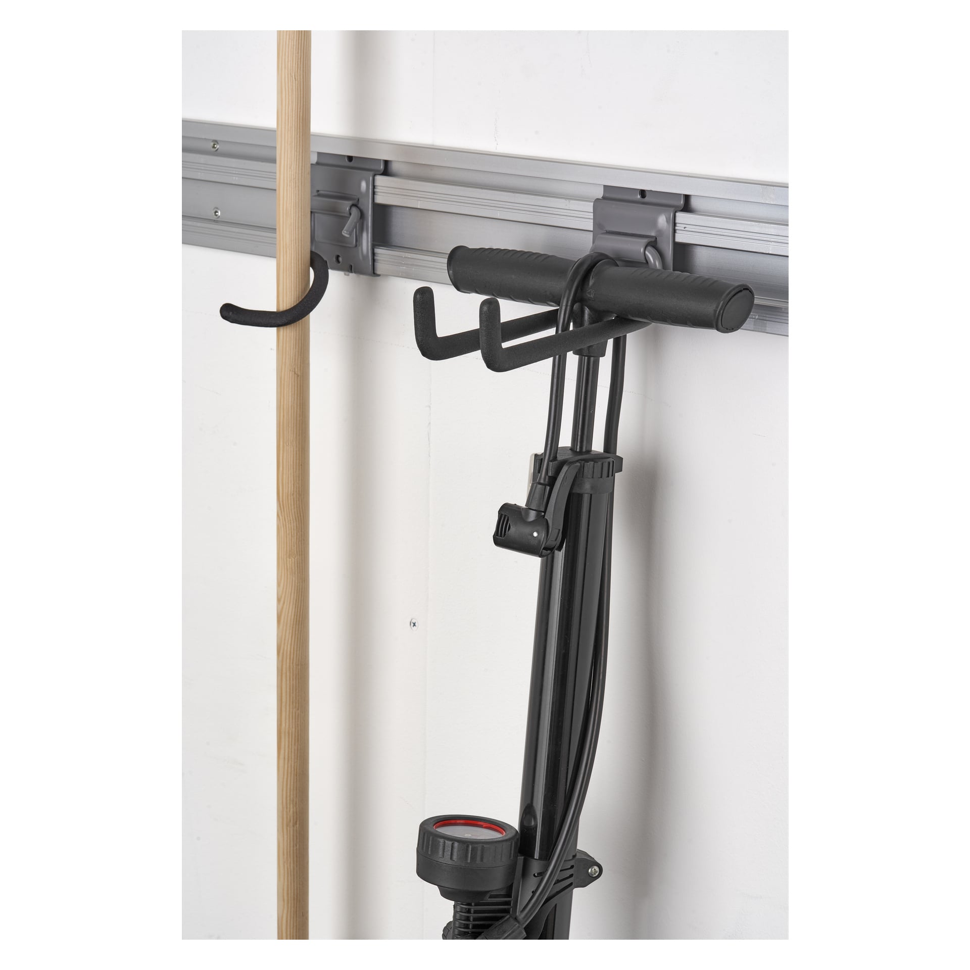 En närbild på Hard Head Tool-kroken, monterad på en vägg i ett garage eller ett tvättrum, som håller ett verktyg med trähandtag bredvid en svart cykelgolvpump.