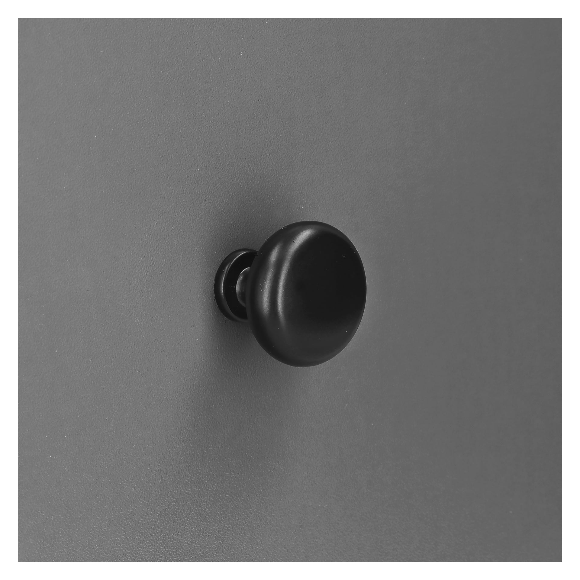 Ett svart, runt "Knob, black 2pack" från Hard Head är fäst på en slät grå yta. Bakgrunden är enkel och fri från andra föremål.