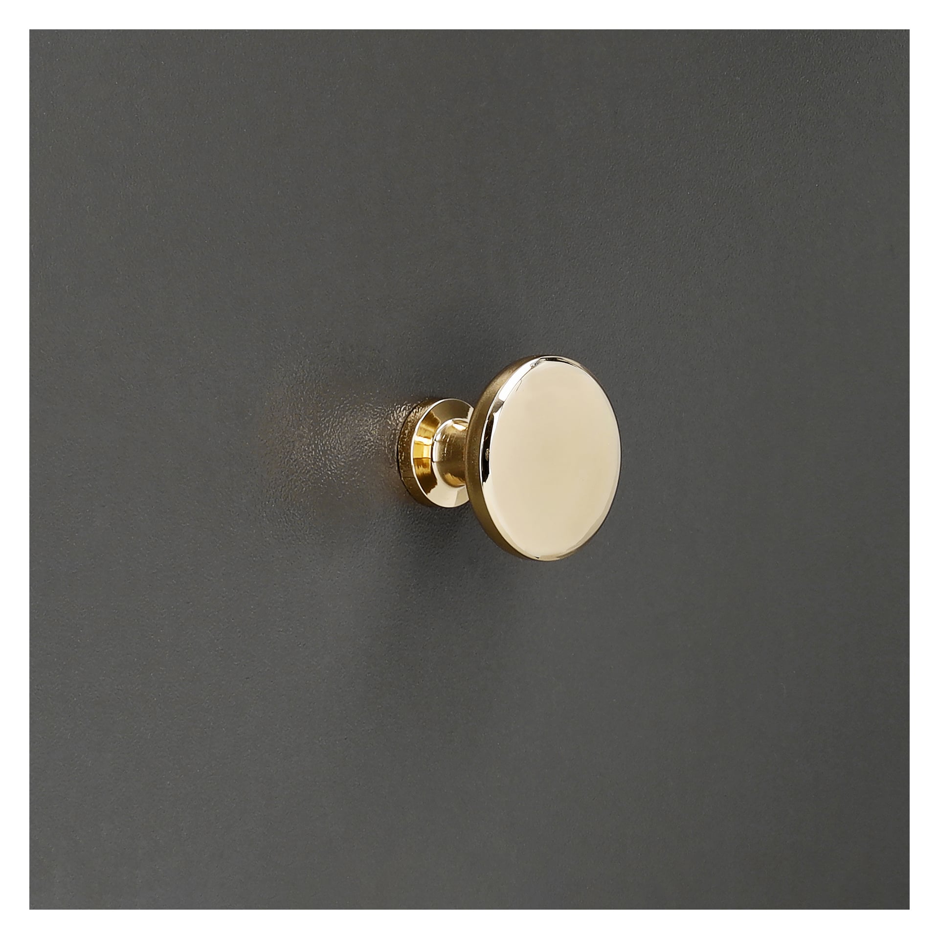 En glänsande, guldfärgad ratt från Hard Head "Knob, guldfärgat 2-pack" är monterad på en slät, mörkgrå yta. Dess enkla form och polerade finish fångar och reflekterar ljuset.