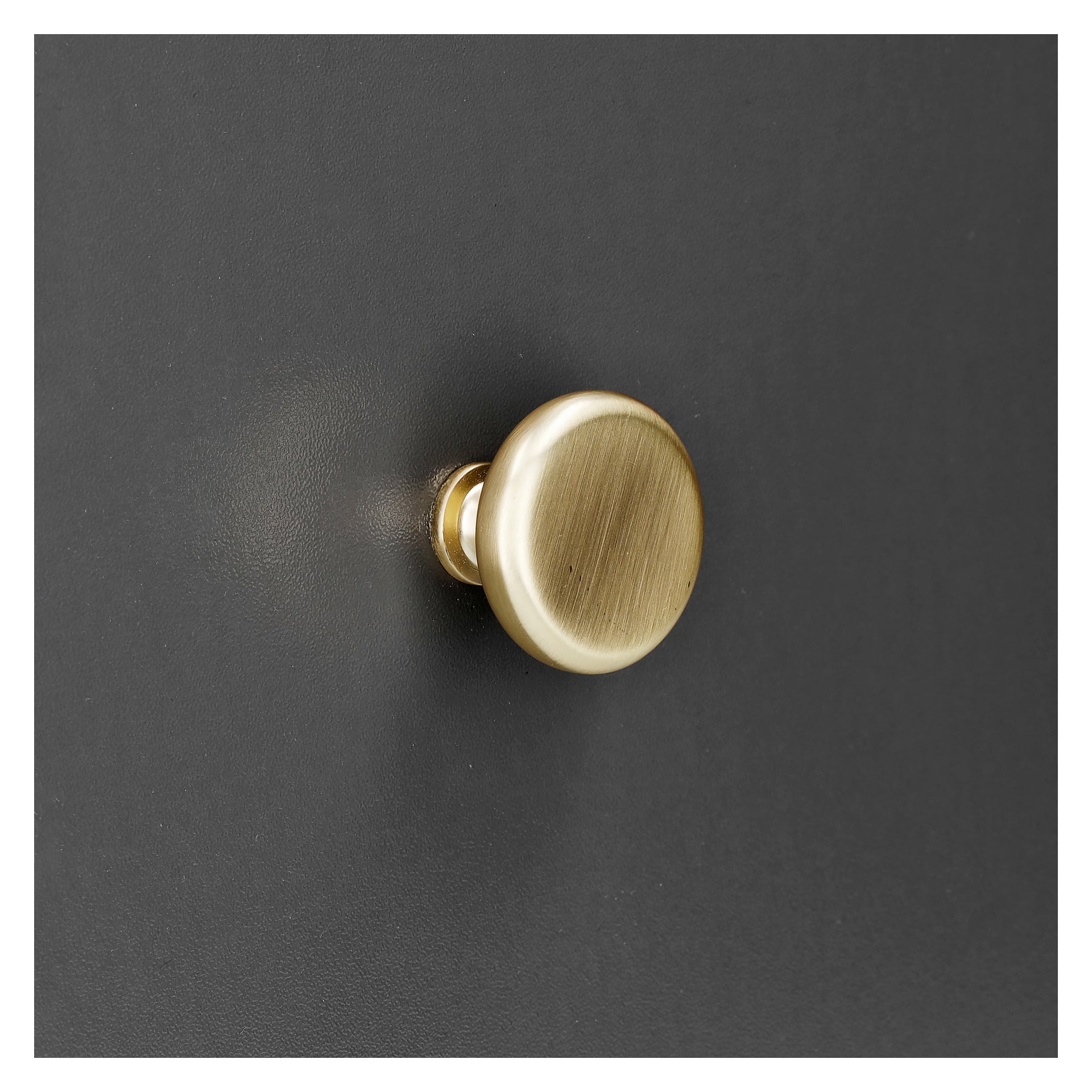 En guldfärgad metallknopp från Hard Head Knob 2-paketet är monterad på en slät, mörkgrå yta. Dess borstade yta glänser i ljuset och framhäver den texturerade designen, med en mjuk skugga synlig till vänster mot en diskret bakgrund.