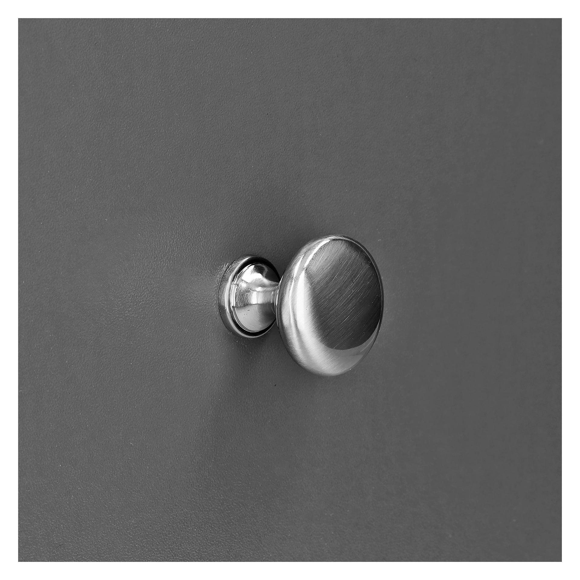 En Hard Head Button från det borstade nickel 2-paketet är installerad på en slank, matt grå bakgrund. Ratten har en borstad metallyta, en rund bas och är fri från synliga markeringar, tangenter eller unika detaljer både på ratten och det omgivande området.