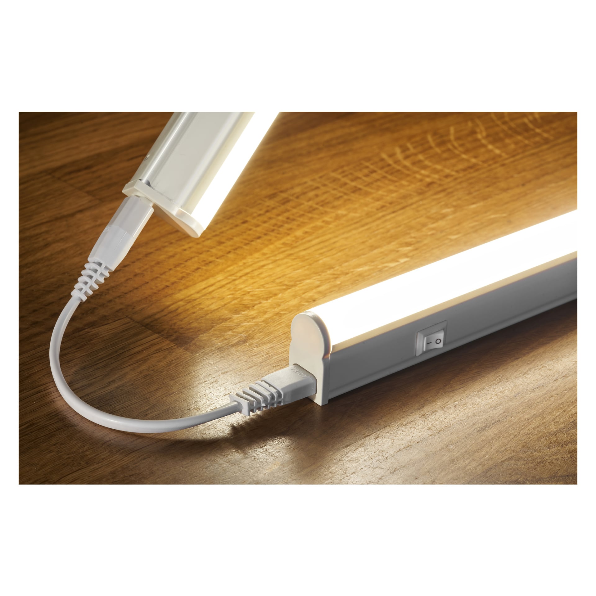 Två Anslut Worktop-lampor med LED-lampor är sammanlänkade med en vit strömkabel på en träyta. Båda lyser starkt, och en har en sidobrytare i sikte.