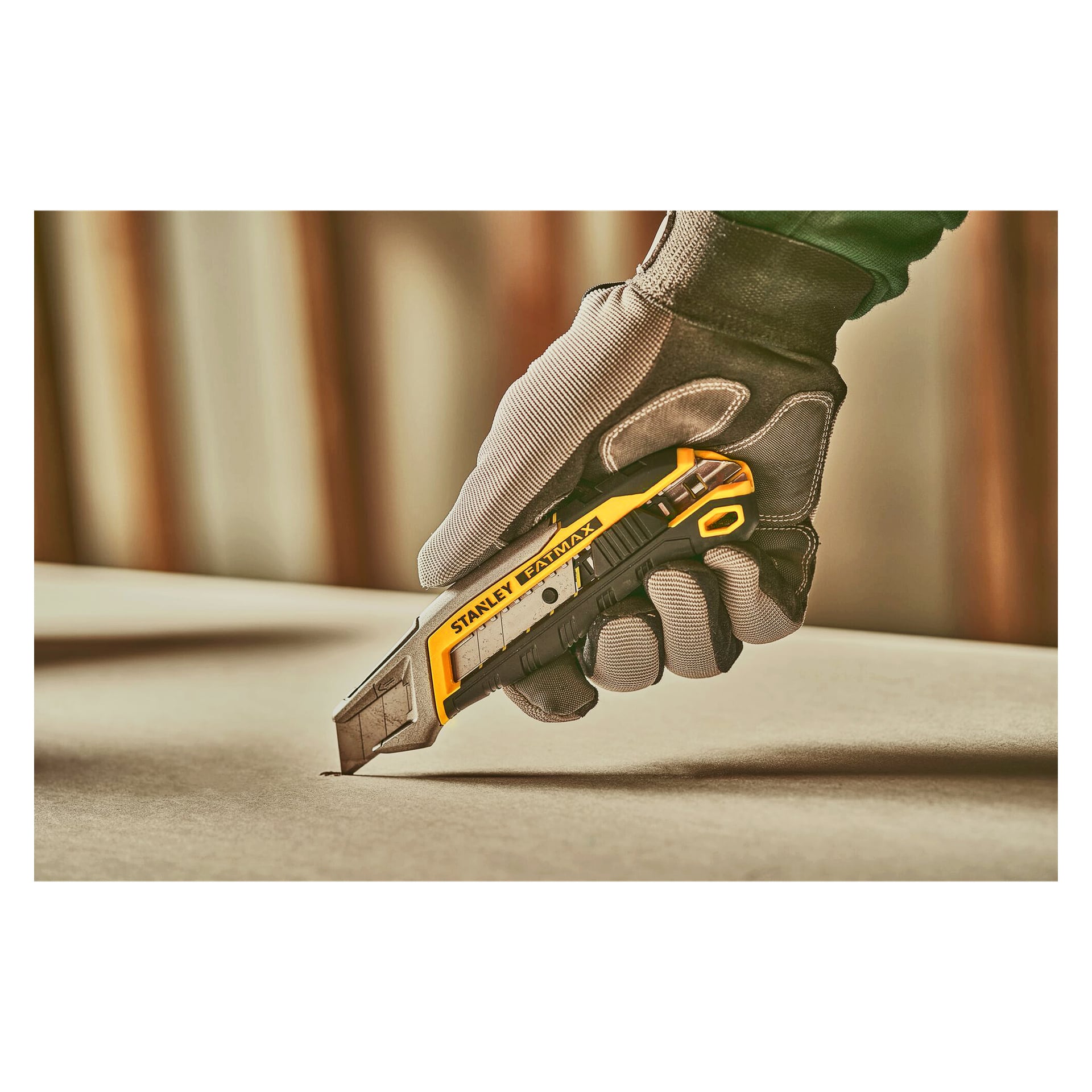 En handskbeklädd hand använder en gul och svart Stanley FatMax hobbykniv för att skära igenom ett ark på en plan yta.