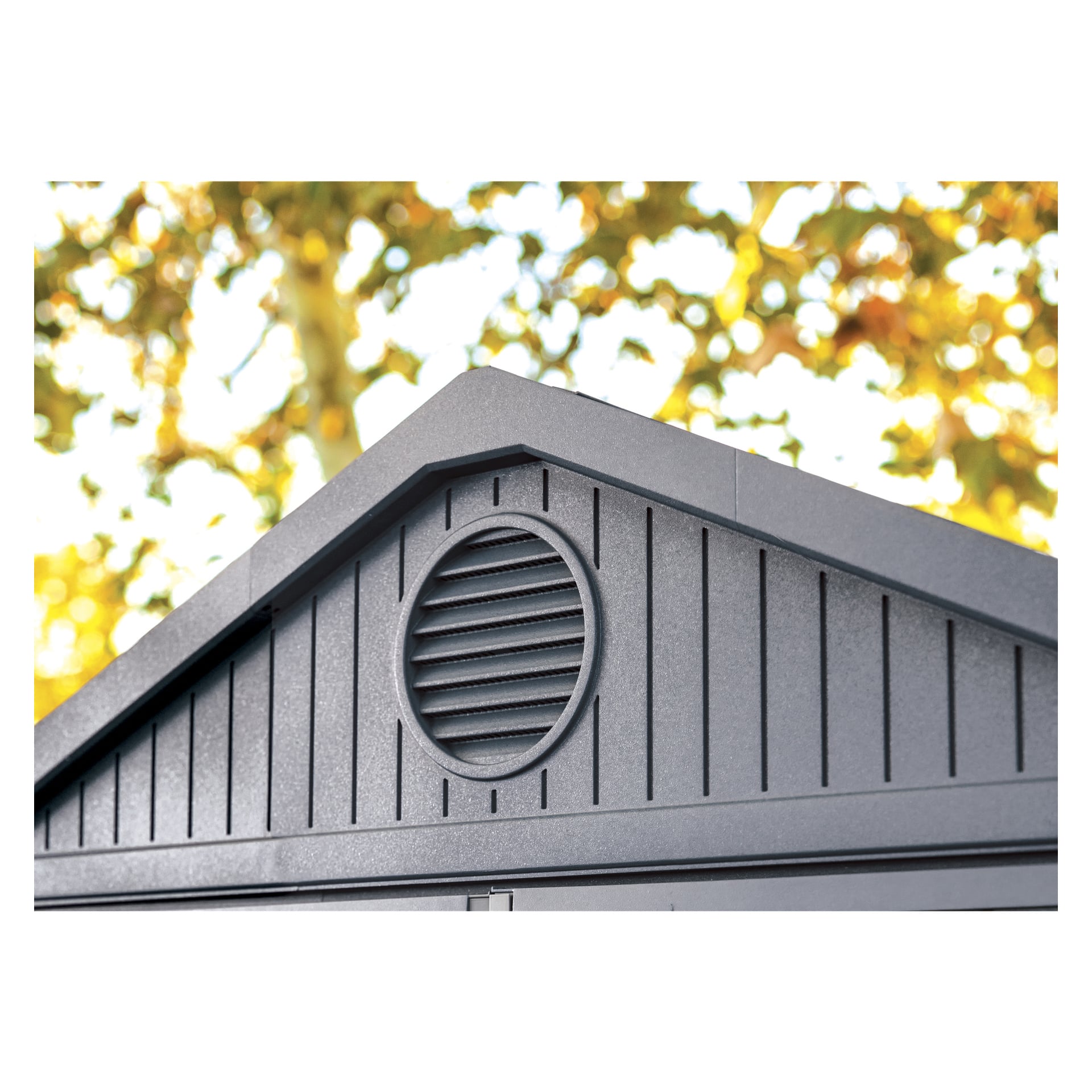 Närbild av den övre delen av Keter Darwin 6x8 Storage Shed med dubbeldörrar, en oval ventilationsöppning med horisontella ribbor och vertikala paneldetaljer, med mjukt suddig grön och gul lövverk i bakgrunden.