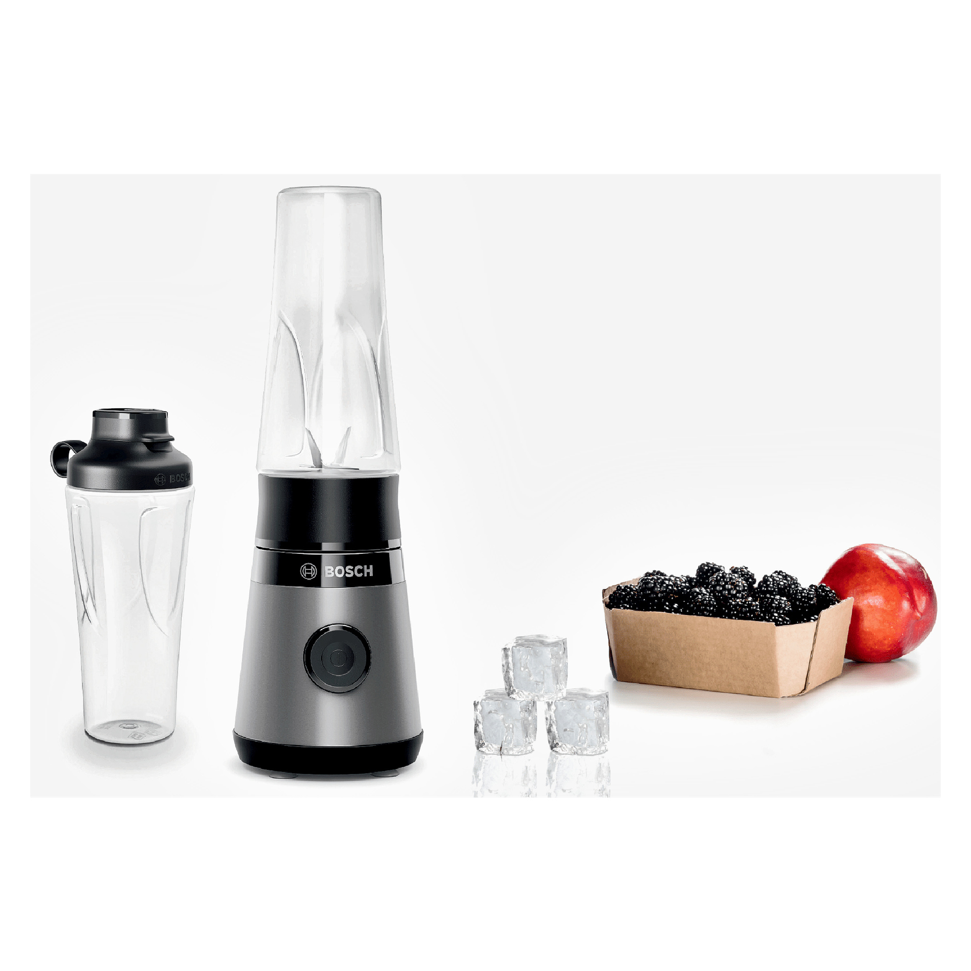 Bosch Home Blender MMB2111S placerad bredvid en tom flaska, fyra isbitar, en björnbärsbehållare och ett rött äpple.