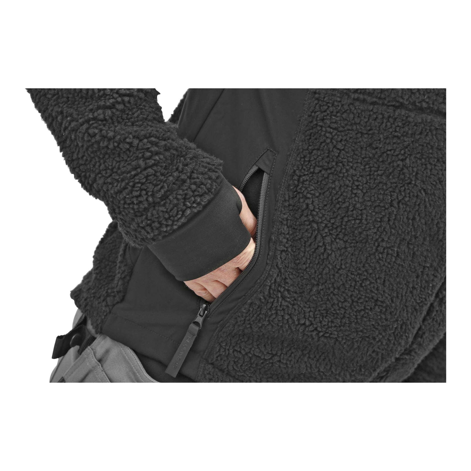 En person klädd i en Bluewear Pro Workwear herrpälsjacka med ett fluffigt, texturerat utseende sträcker sig in i den dragkedjaförsedda sidofickan med höger hand. De har också grå byxor på sig.