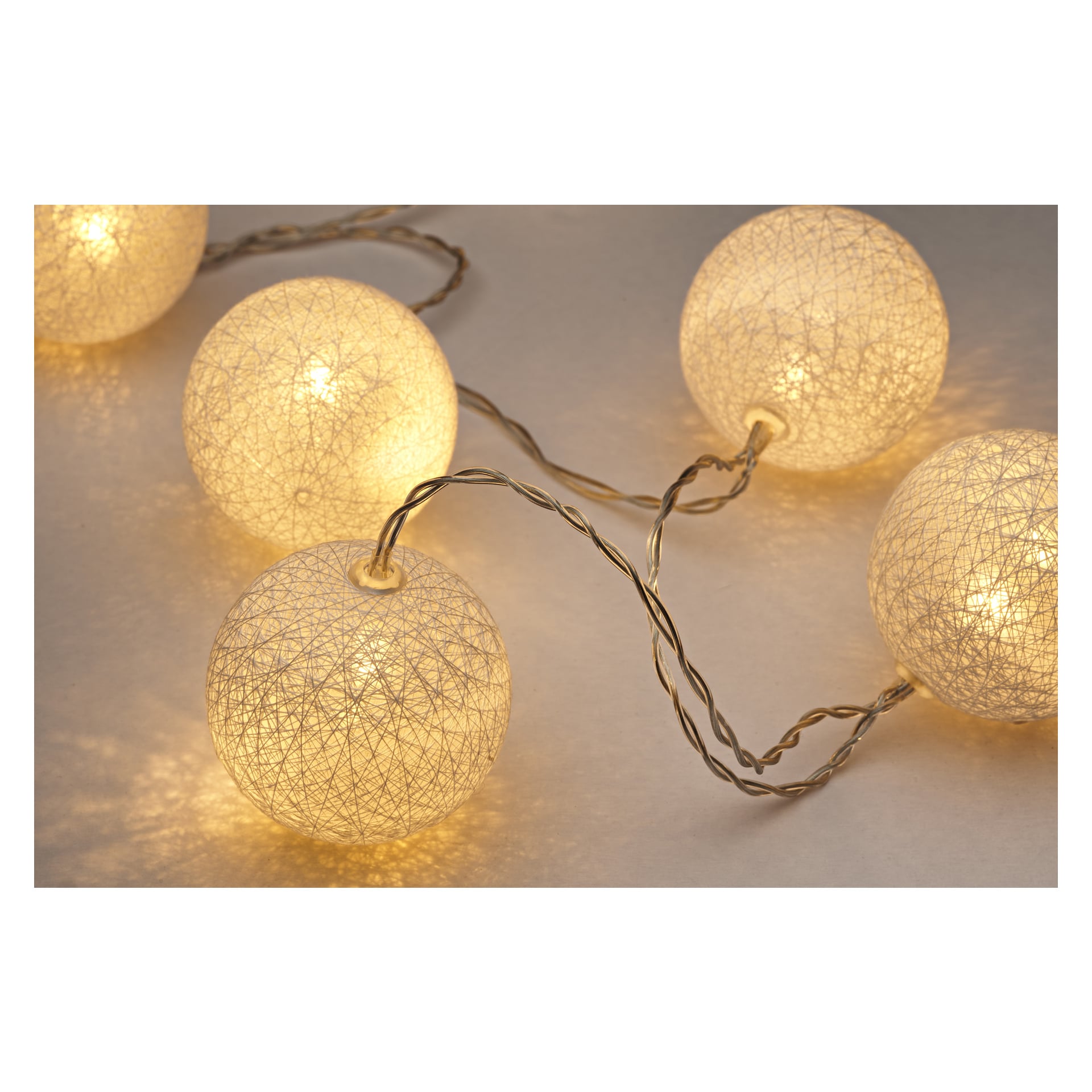 Fem EKVIP LED-ljusslingor med texturerade, runda ytor är sammanfogade med en tvinnad sladd, som lyser i ett varmt gult ljus och skapar mjuka skuggor.