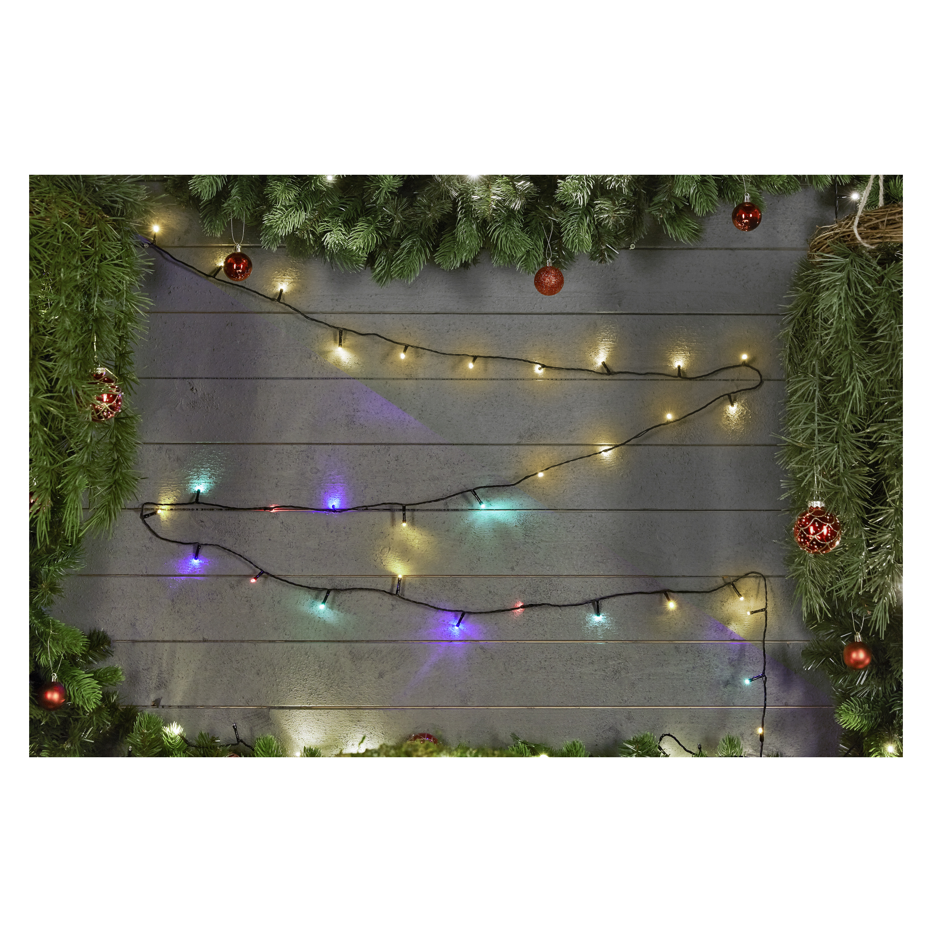 Eine grau gestrichene Holzwand ist mit grünen Kieferngirlanden, roten Ornamenten und zwei EKVIP batteriebetriebenen LED-Lichterketten geschmückt – eine mit mehrfarbigen Glühbirnen, die andere mit warmgelben Lampen.