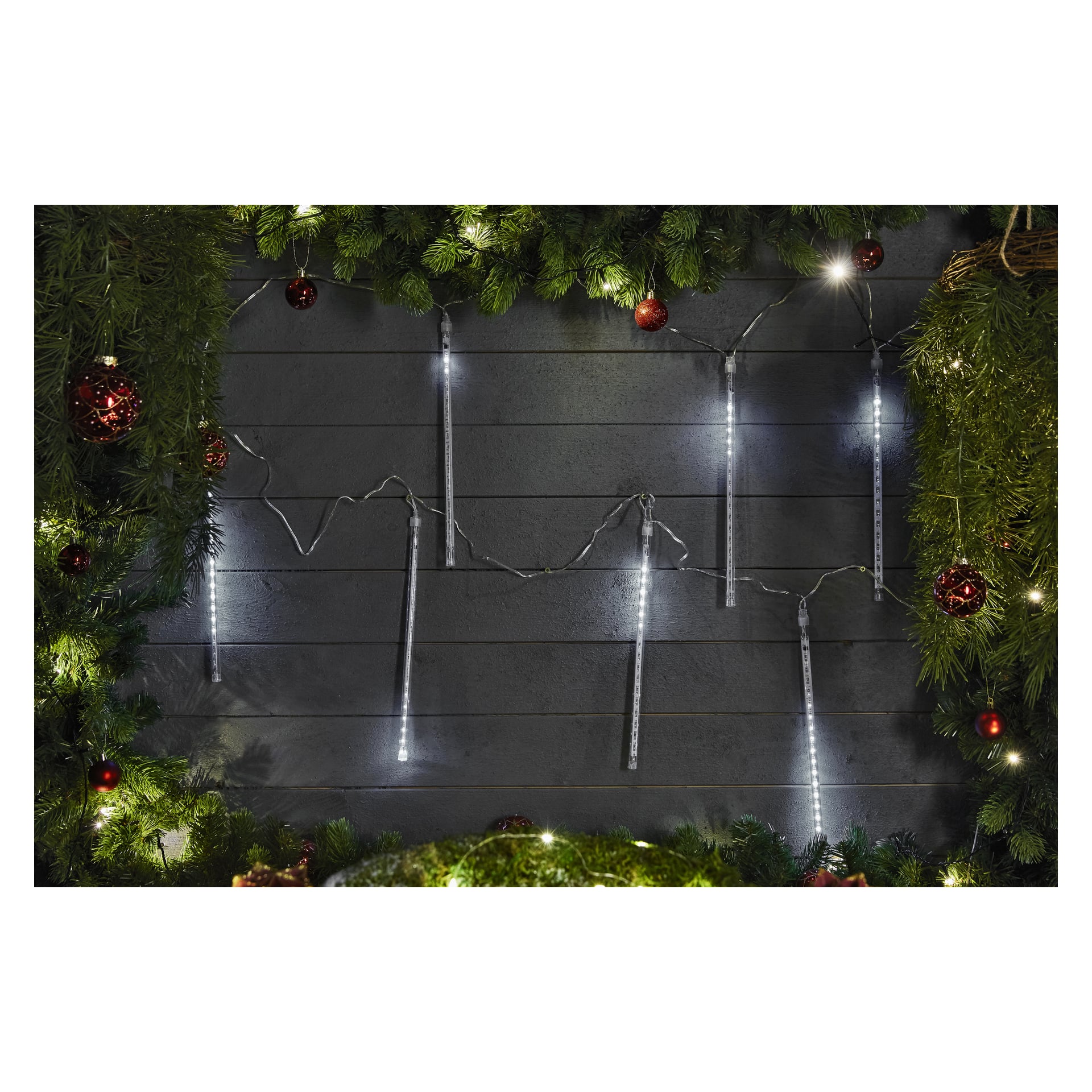 EKVIP LED-meteorisade Connectable System -valot on ripustettu tumman puuseinän varrella, loistaen kirkkaasti vihreiden mäntyseppeleiden ja punaisten koristeiden lomassa juhlatunnelmaa.