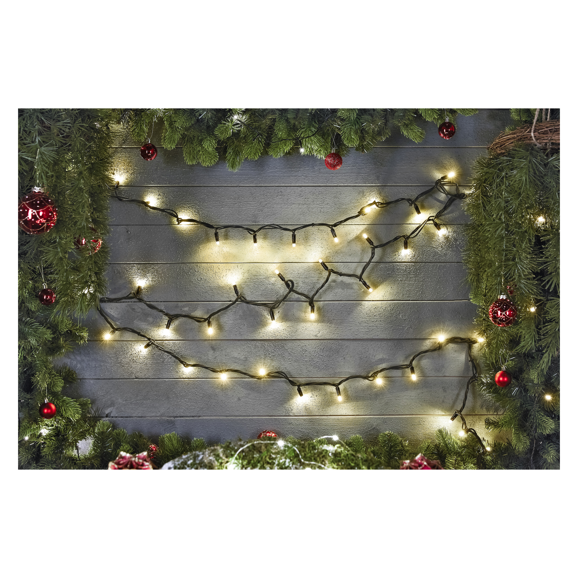 EKVIP LED-ljusslingor från Connectable System hänger längs en grå trävägg, omgiven av gröna tallgirlanger och röda prydnader, vilket ger rummet en glad julkänsla.