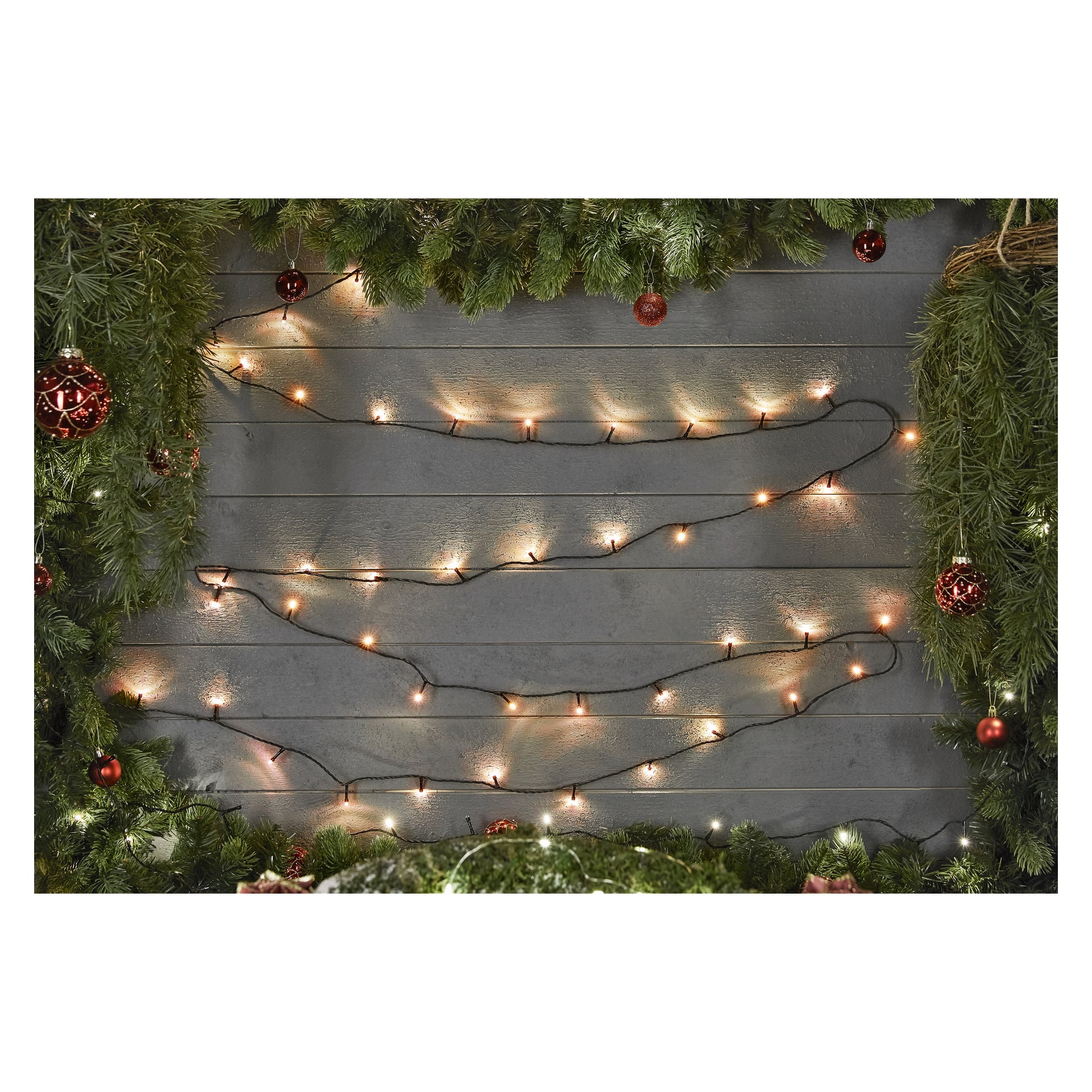Grå trävägg dekorerad med EKVIP LED-slingor, inramad av frodiga gröna tallgirlanger och klarröda prydnader för en festlig julkänsla.