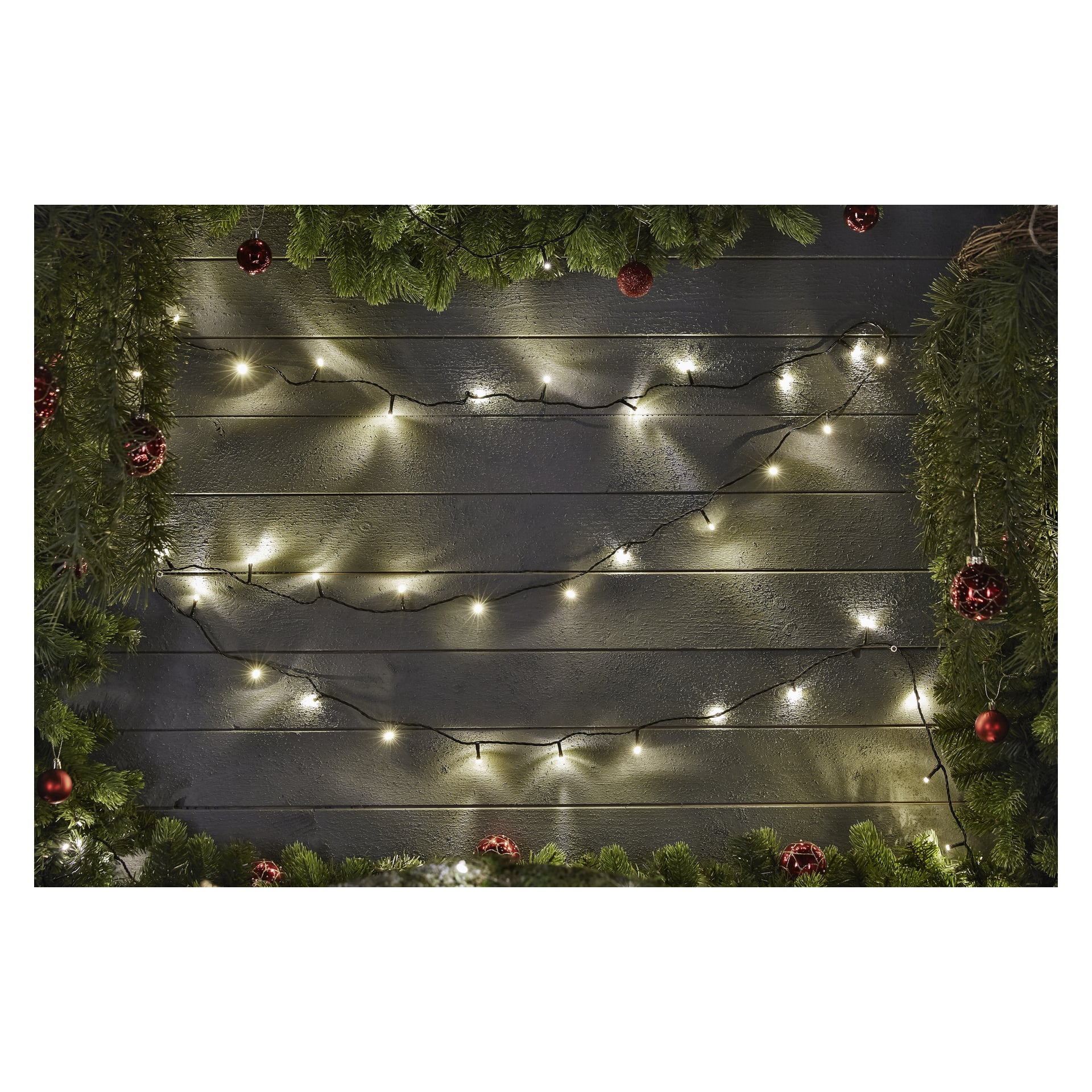 EKVIP LED-ljusslingor hänger längs en mörk trävägg, omgiven av gröna tallgirlanger och röda ornament upptill, på sidorna och undersidan för en festlig julkänsla.