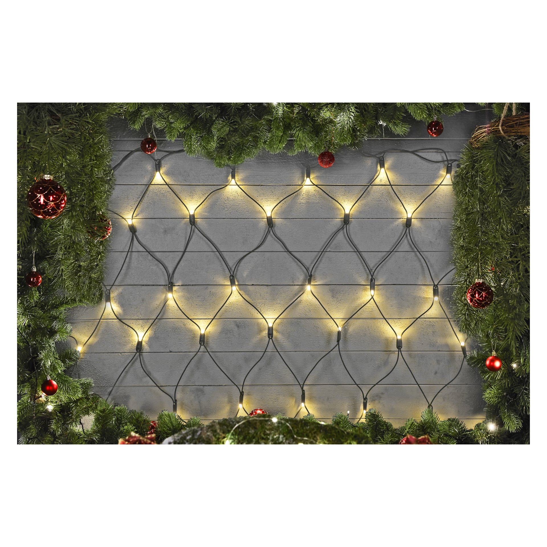 Gula LED-lampor från EKVIP Connectable System bildar ett lysande nät över en trävägg. Scenen ramas in längs toppen och sidorna av gröna tallgrenar och röda julgransprydnader, vilket ger den ett glatt julintryck.