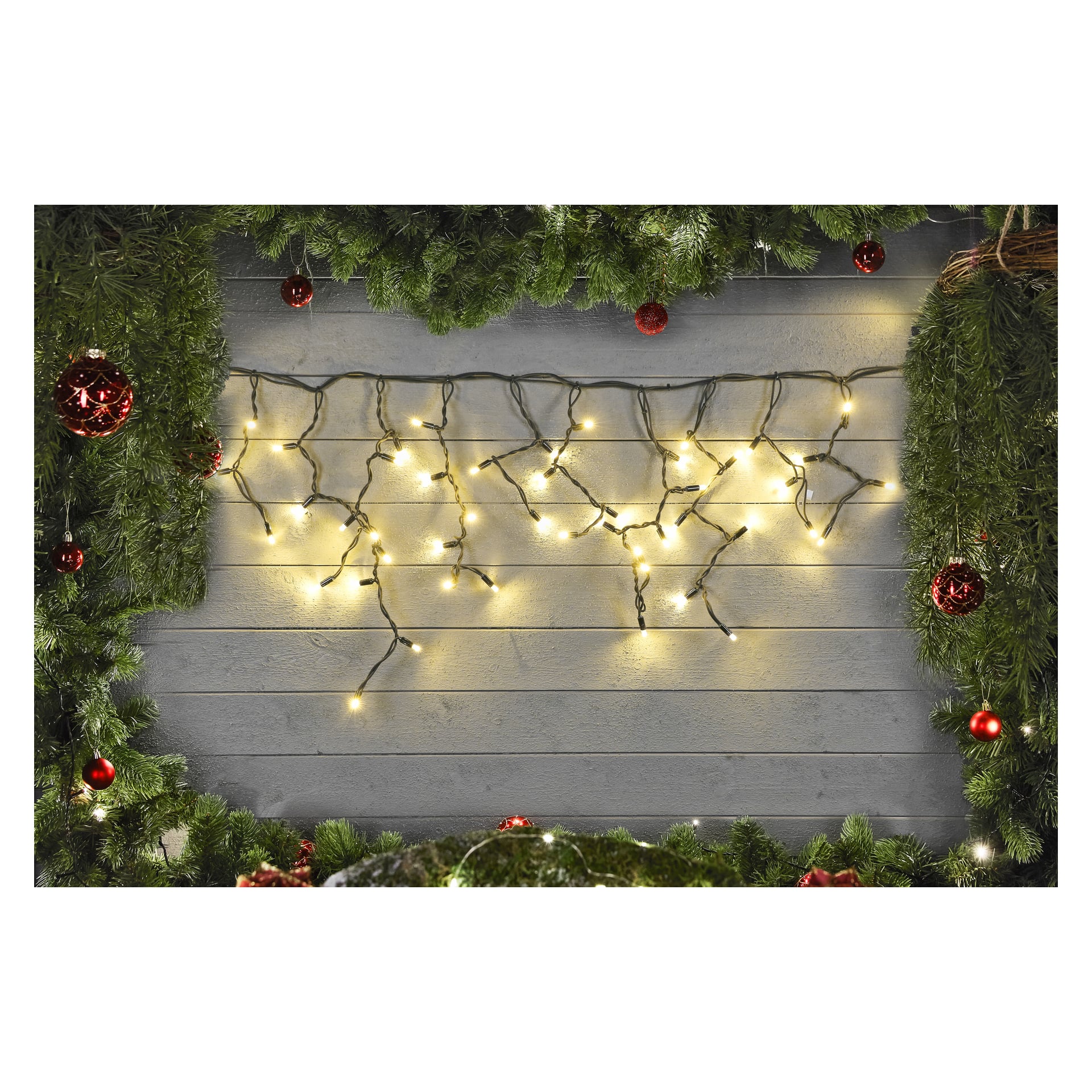 Gröna girlander dekorerade med röda ornament ramar in en grå trävägg, upplyst av EKVIP:s LED-istappssträng Connectable System. De lysande ljusen skapar en varm och festlig julstämning i centrum.