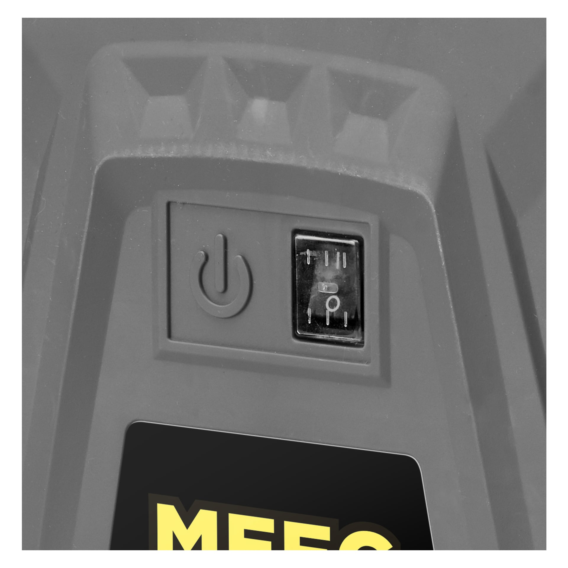 En detaljerad vy visar en strömknapp och en treinställningsknapp på den grå plastytan på en Meec Tools-kompressor. Strömbrytaren har positioner markerade I, II och en ikon som ser ut som en vattendroppe. Nedan kan en del av en etikett med gul text ses.