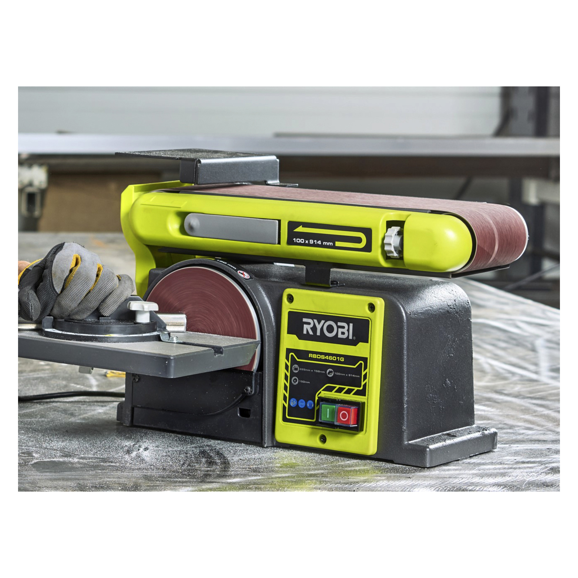 En Ryobi RBDS4601G bånd-/skivesliper opererer på et arbeidsbord, med støv på overflaten. En person med hansker justerer gjæringsmåleren ved skivesliperen.