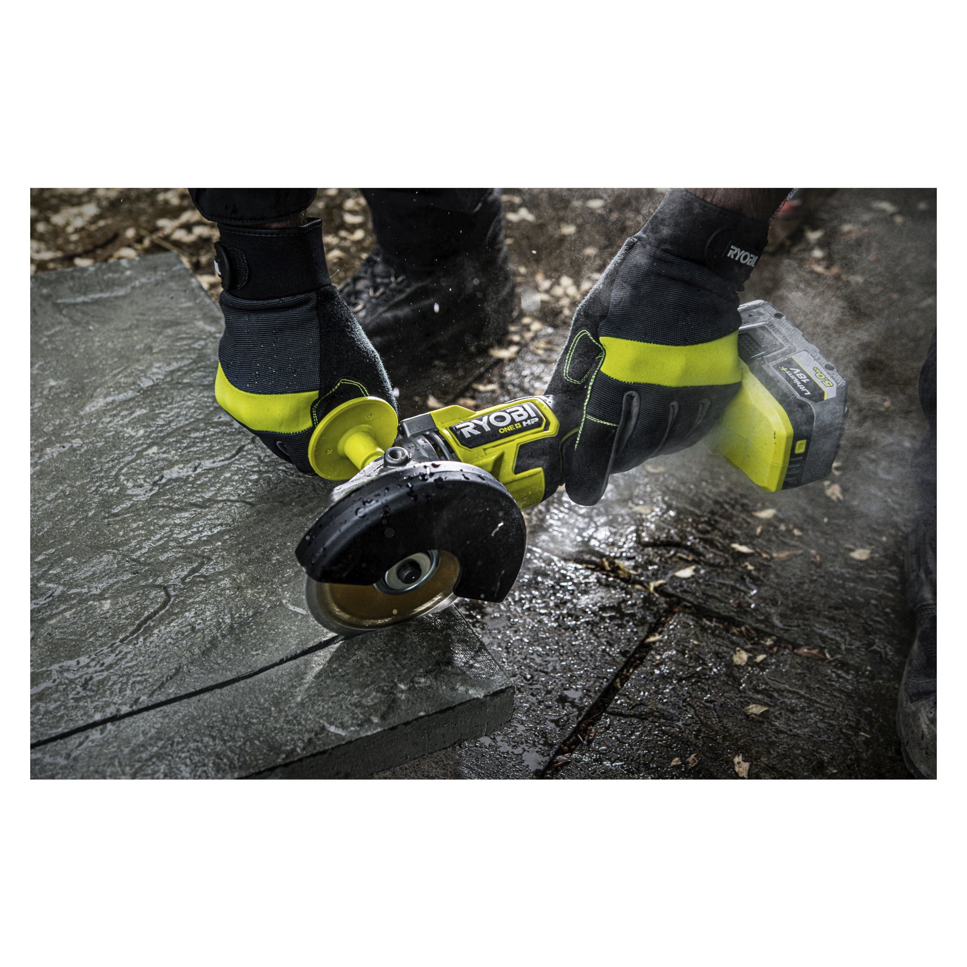 En person i svarta och gula handskar använder Ryobi One+ HP vinkelslipmaskin RAG18X-140SJ för att skära i en betongplatta, vilket skapar damm med utspridda löv och kakel på marken.