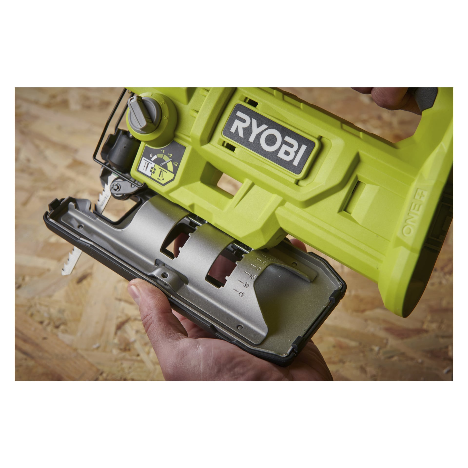 En detaljerad vy av någon som justerar bottenplattan på en Ryobi One+ batteridriven sticksåg RJS18-0, med fokus på var händerna är placerade och de synliga mätmarkeringarna på verktyget, mot en träbakgrund.
