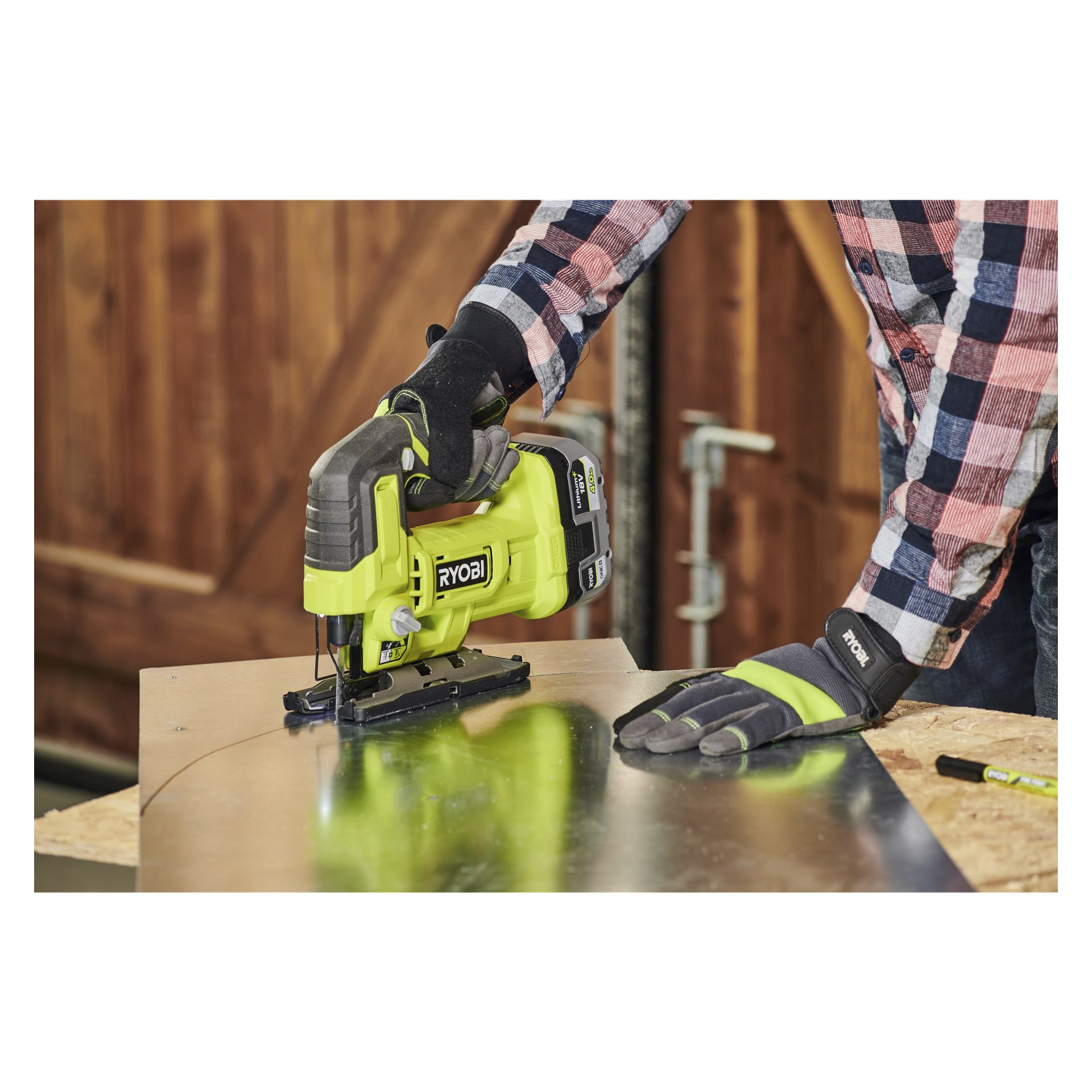 Med handskar och rutig skjorta använder man en Ryobi One+ batteridriven sticksåg RJS18-0 för att skära en kurva i en metallplåt placerad på trä, med en penna liggande i arbetsytan.