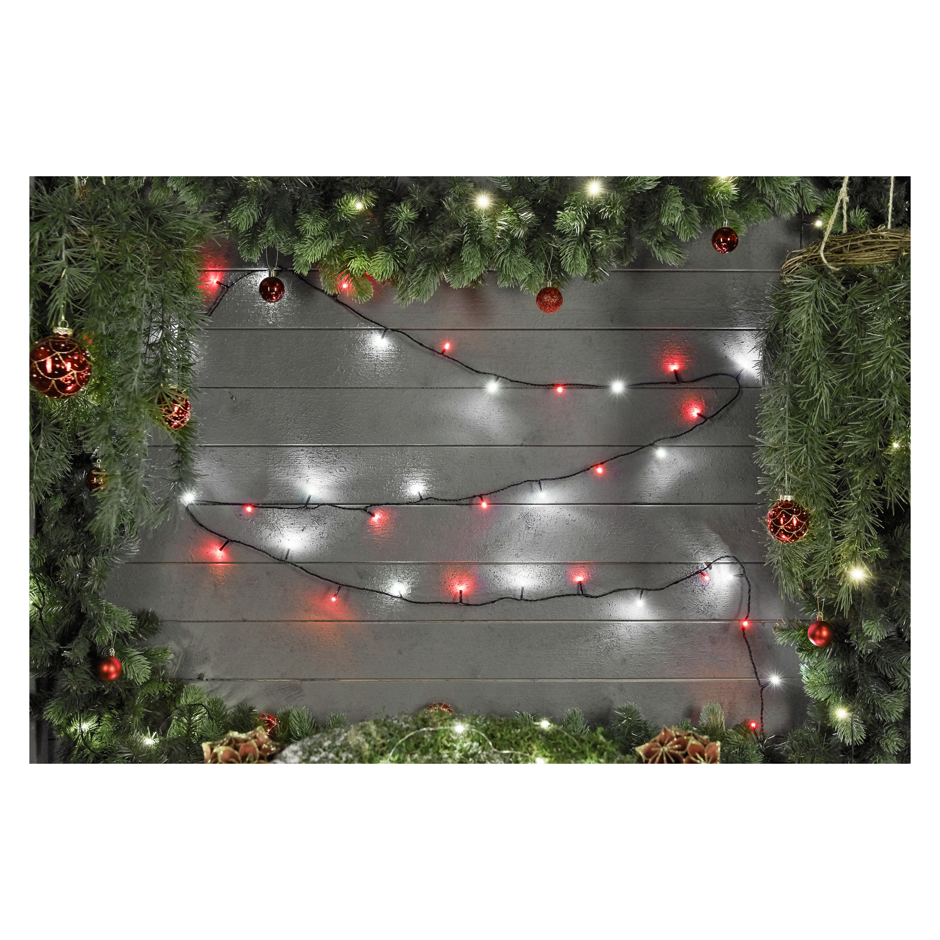 Frodiga gröna tallgirlanger dekorerade med klarröda ornament och en rad EKVIP LED-lampor i rött och vitt pryder den grå träväggen. Girlanderna ramar in toppen och sidorna och skapar en glädjefylld julscen.