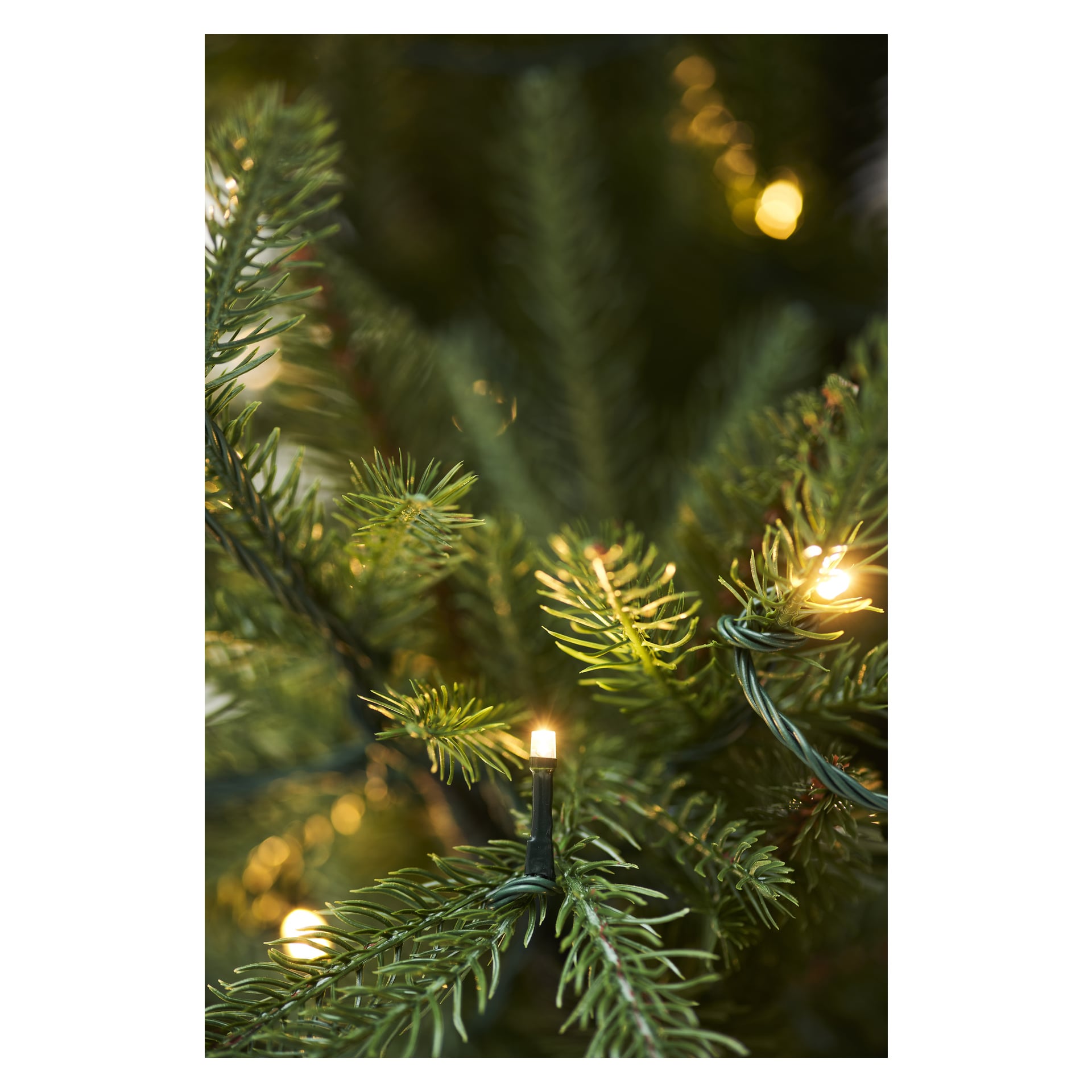 Detaljerad vy av EKVIP Lifelike Christmas Tree som visar dess livfulla gröna grenar dekorerade med integrerade LED-lampor; De varmvita lamporna är tända och lyser mjukt upp de realistiska nålarna.