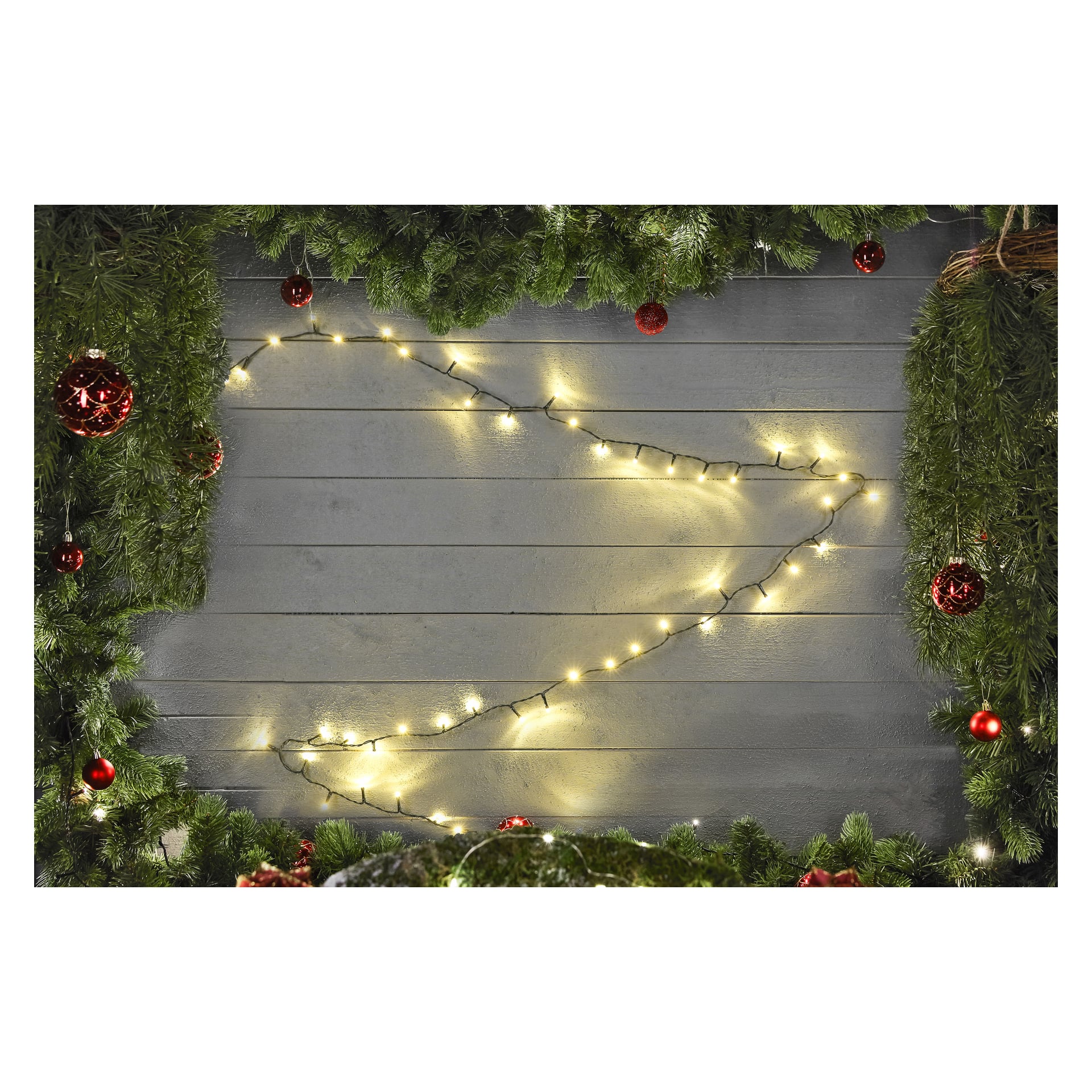 Gröna tallgrenar och röda ornament ramar in en grå trävägg, med EKVIP LED-ljusslingor hängande i ett löst zickzackmönster längs mitten.
