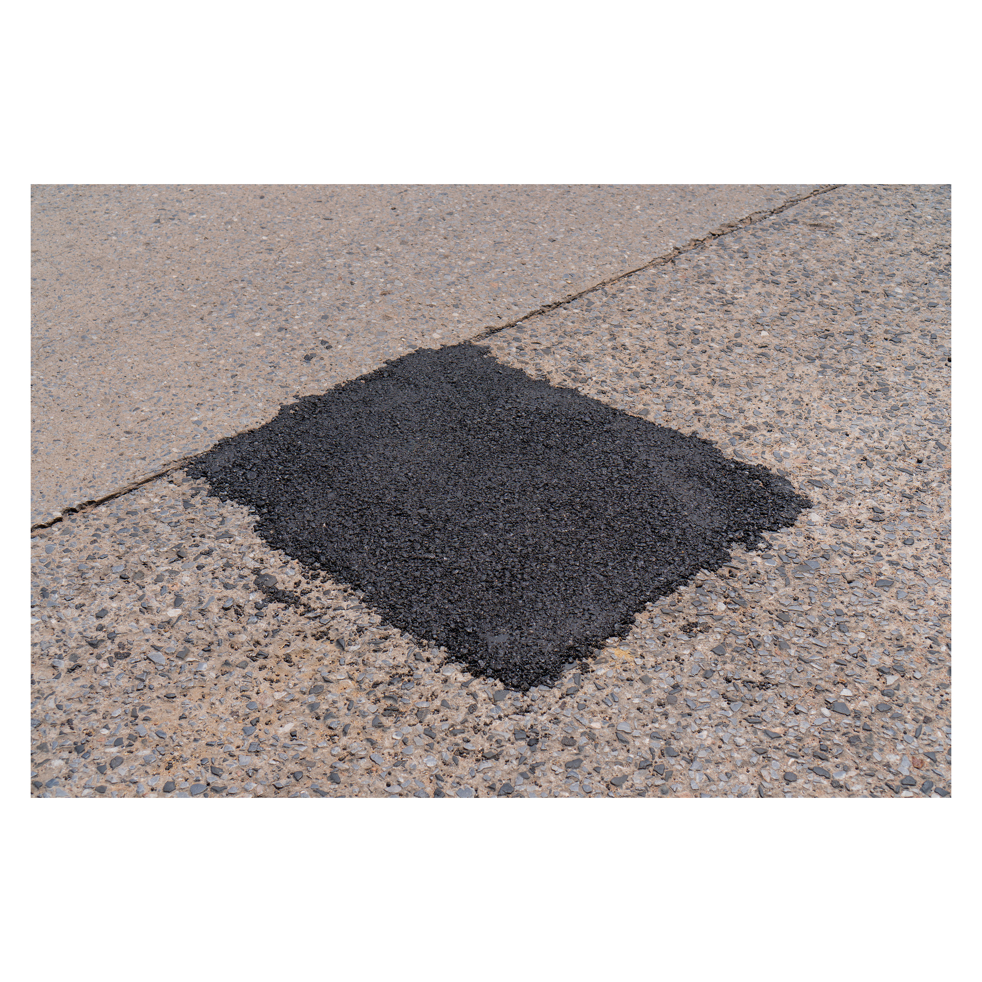 En nyapplicerad, fyrkantig yta av Hard Head Asphalt-reparation kontrasterar mot den lättare, grova betongbeläggningen och framhäver ett område med nyligen underhåll av ytan.