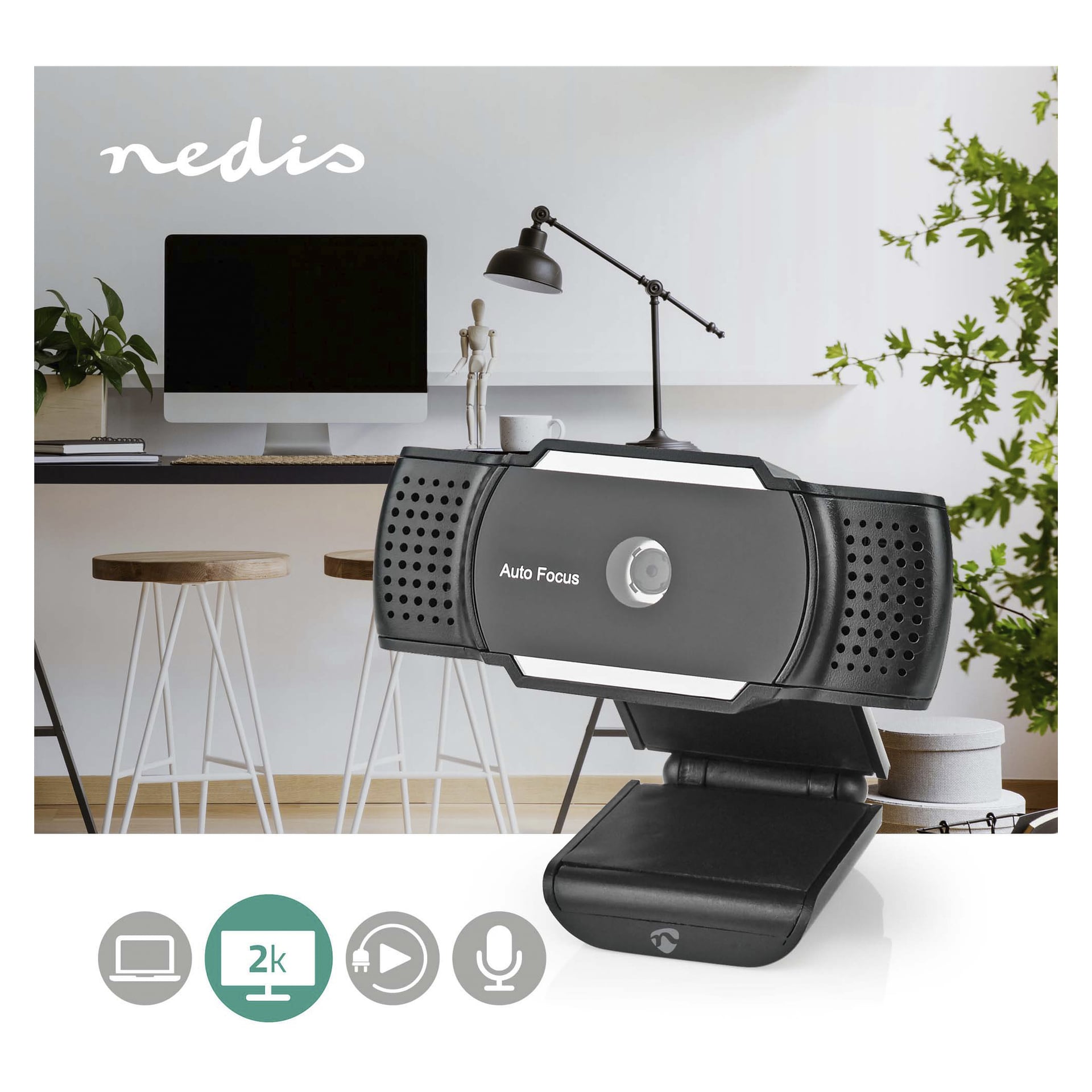 Den svarta Nedis Webcam-WCAM110BK med autofokus visas placerad framför ett modernt kontorsskrivbord som inkluderar dator, lampa, växter och pallar. Ikoner under webbkameran visar dess 2K-upplösning, inbyggda mikrofon och breda kompatibilitet.