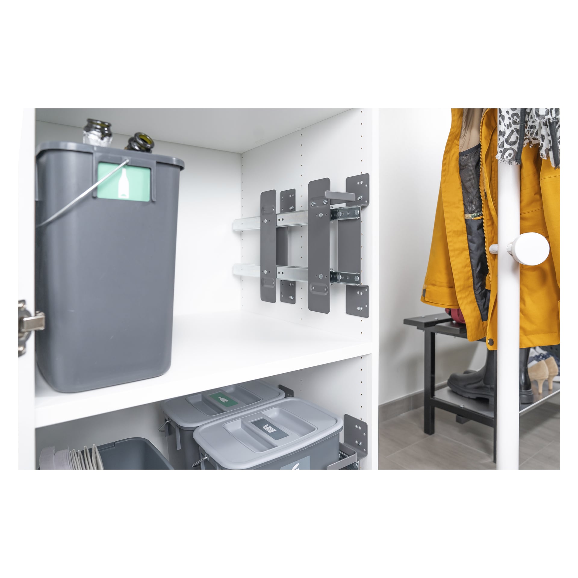 Bilden visar ett Nordiska Plast Pull-out Sorting at Source 6-delat återvinningssystem, som inkluderar vita skåp med grå återvinningskärl arrangerade på hyllorna och ett metallbeslag på väggen monterat inuti. I närheten hänger en gul rock över en vit klädhängare, och en del av en skobänk kan ses i bakgrunden.